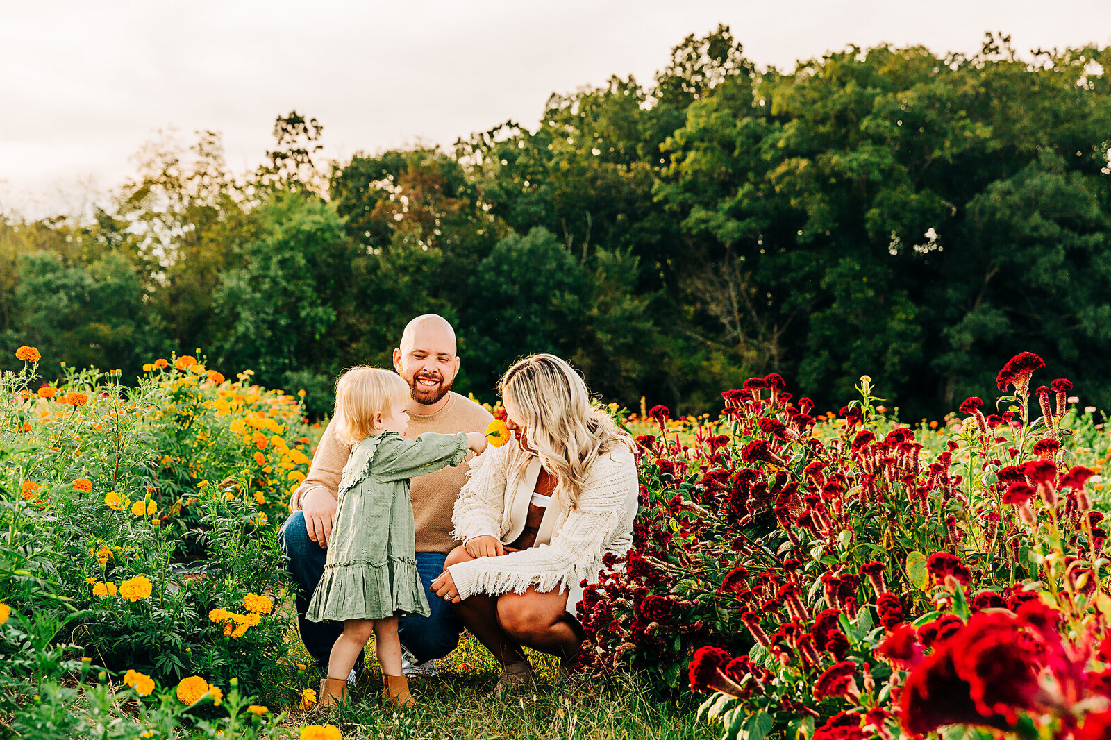 parents squatting down with little girl smelling flowers