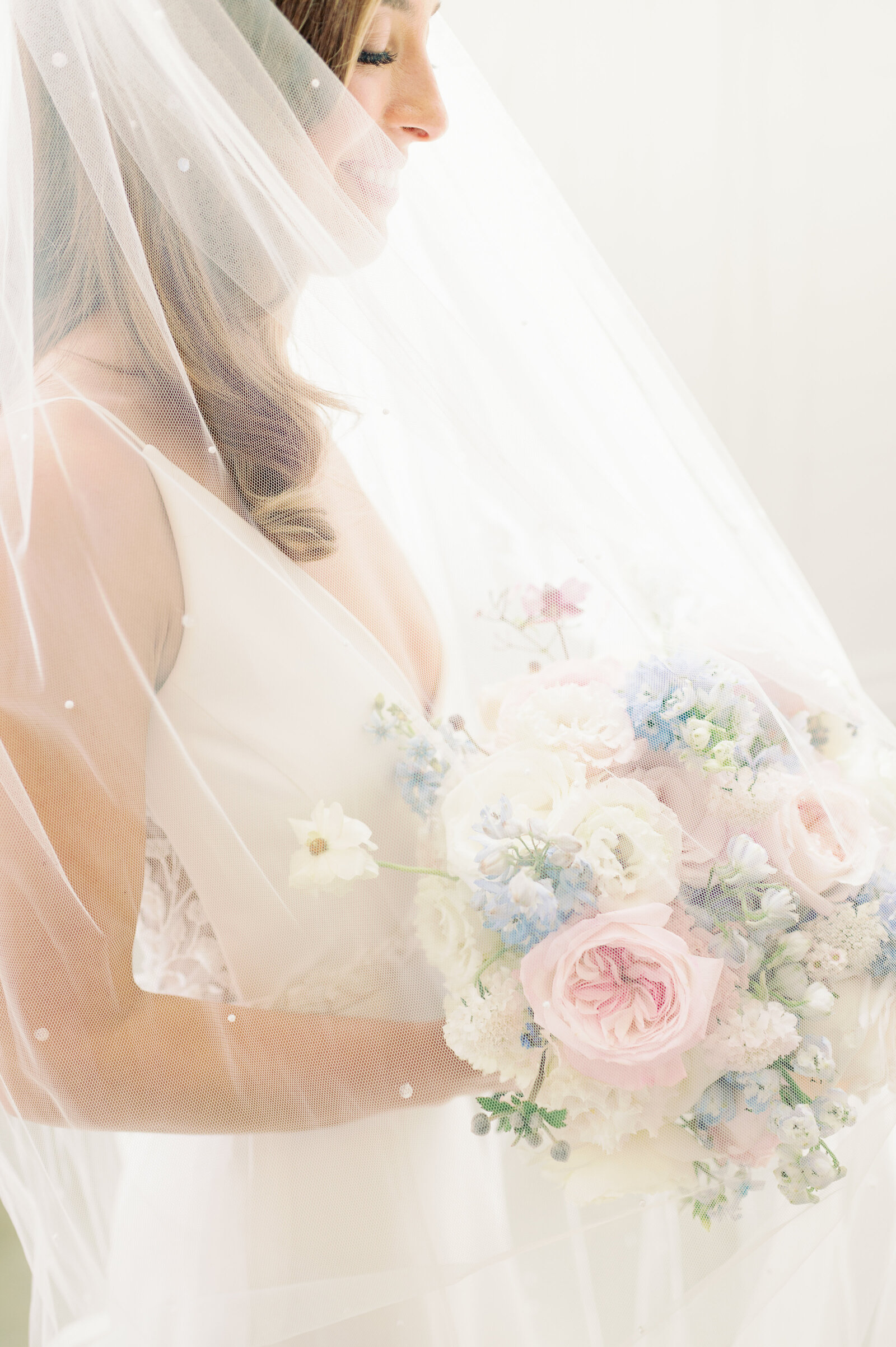 light streaming through a bride's veil as she looks down at the flower bouquet she is holding