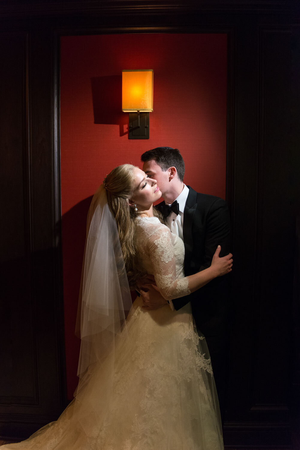 A bride and groom kissing in front of a red wall