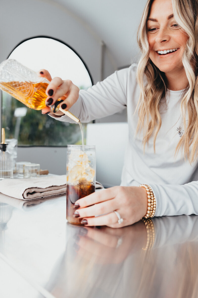 gorgeous woman pouring sweetener into an iced coffee