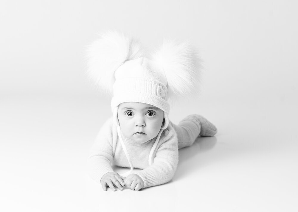 high-key-black-and-white-picture-of-little-girl-laying-on-belly-with-fuzzy-hat