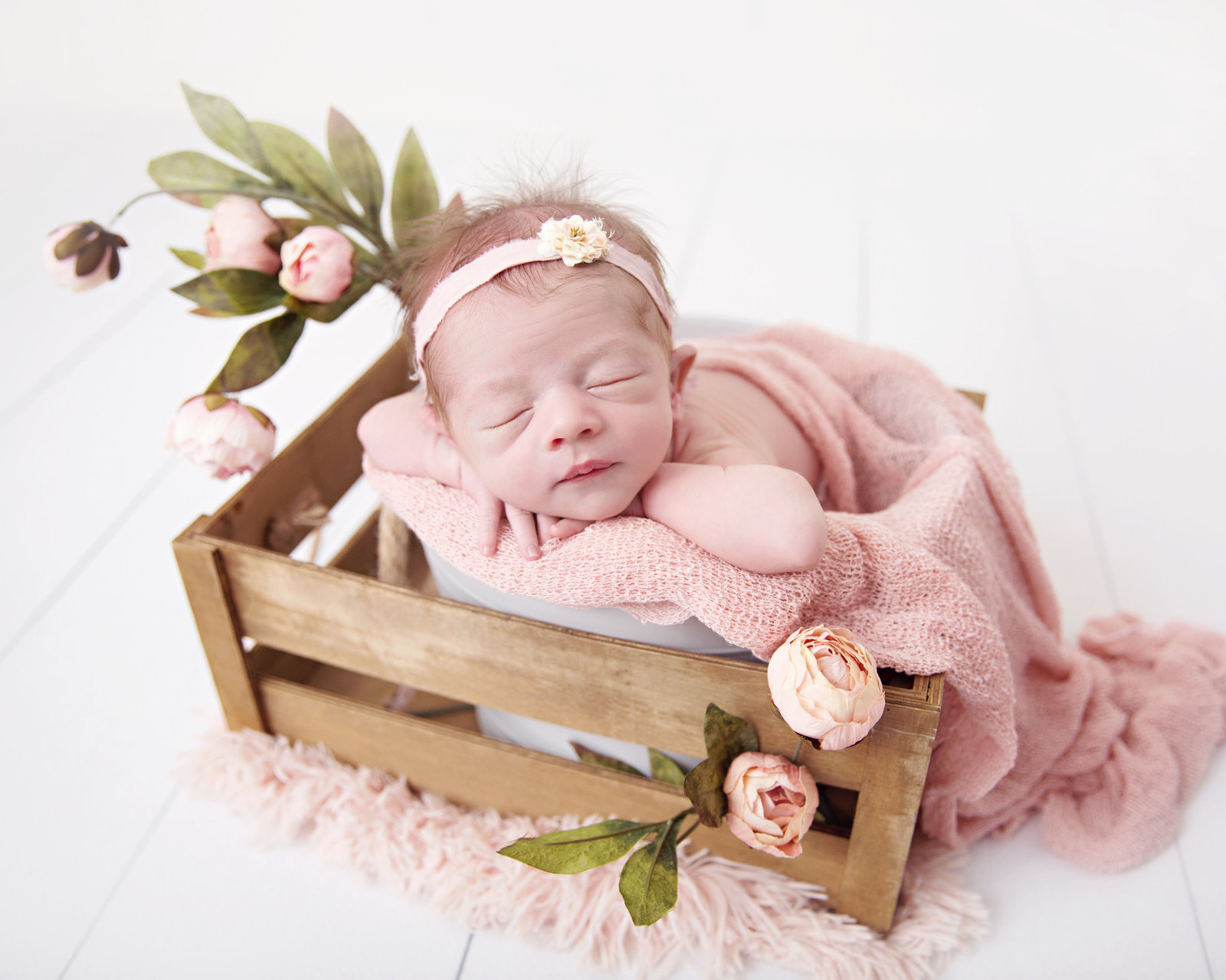 sleeping newborn baby girl with pink flowers in bucket and wooden crate