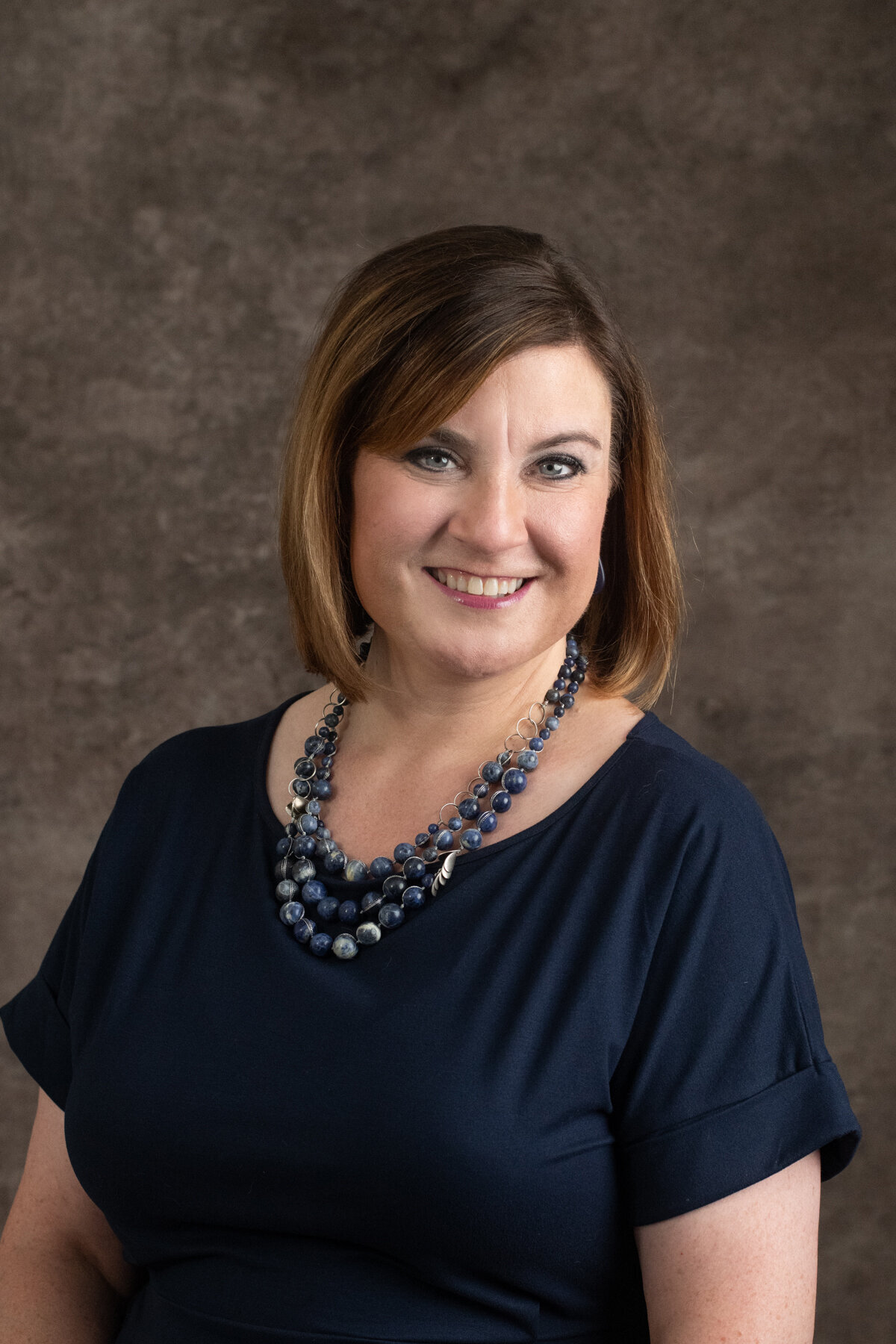 woman smiles in traditional headshot on brown backdrop