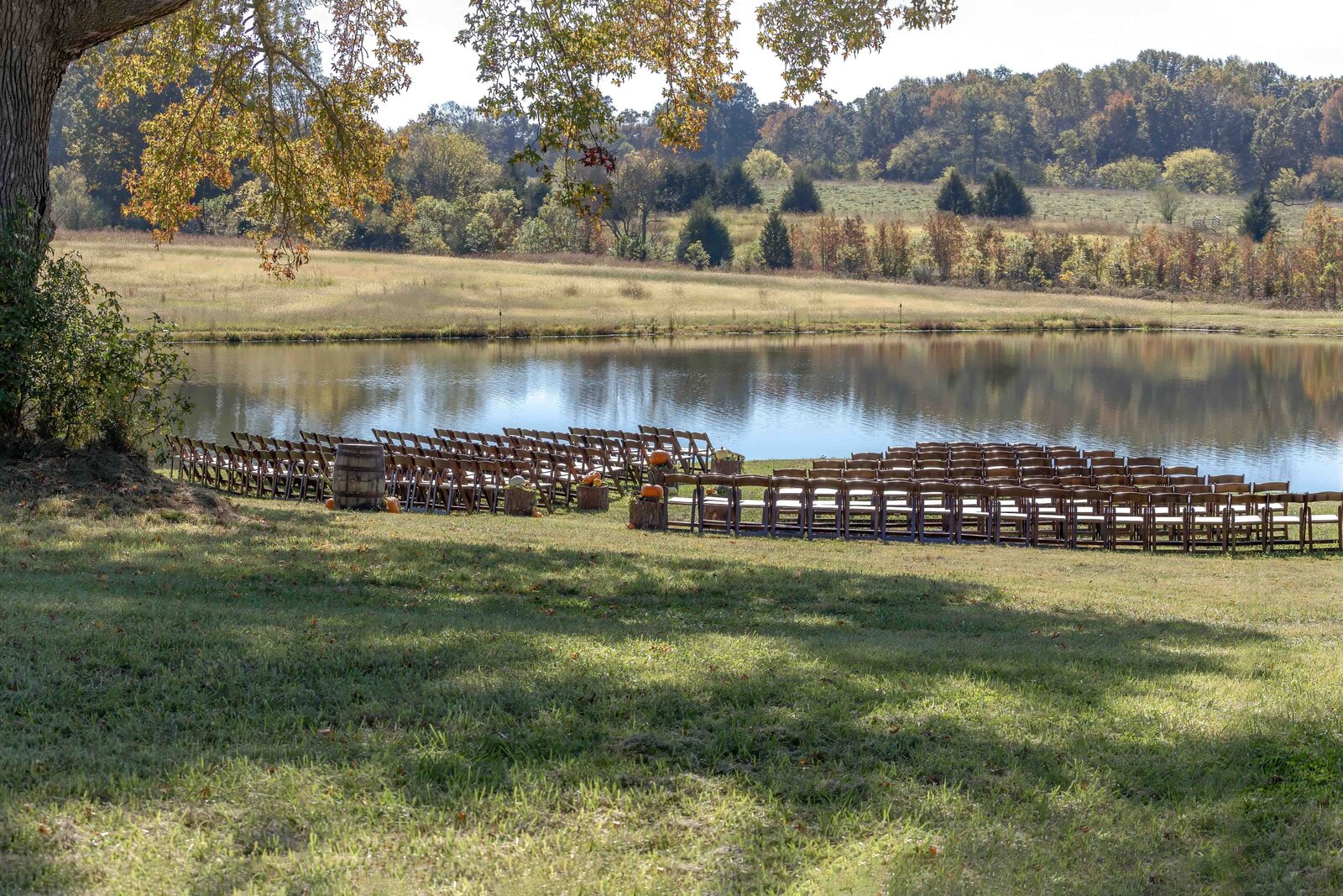 Rows of wooden chairs arranged by a serene pond with fall foliage in the background, captured at an outdoor Boone, NC wedding, blending rustic charm with natural elegance.