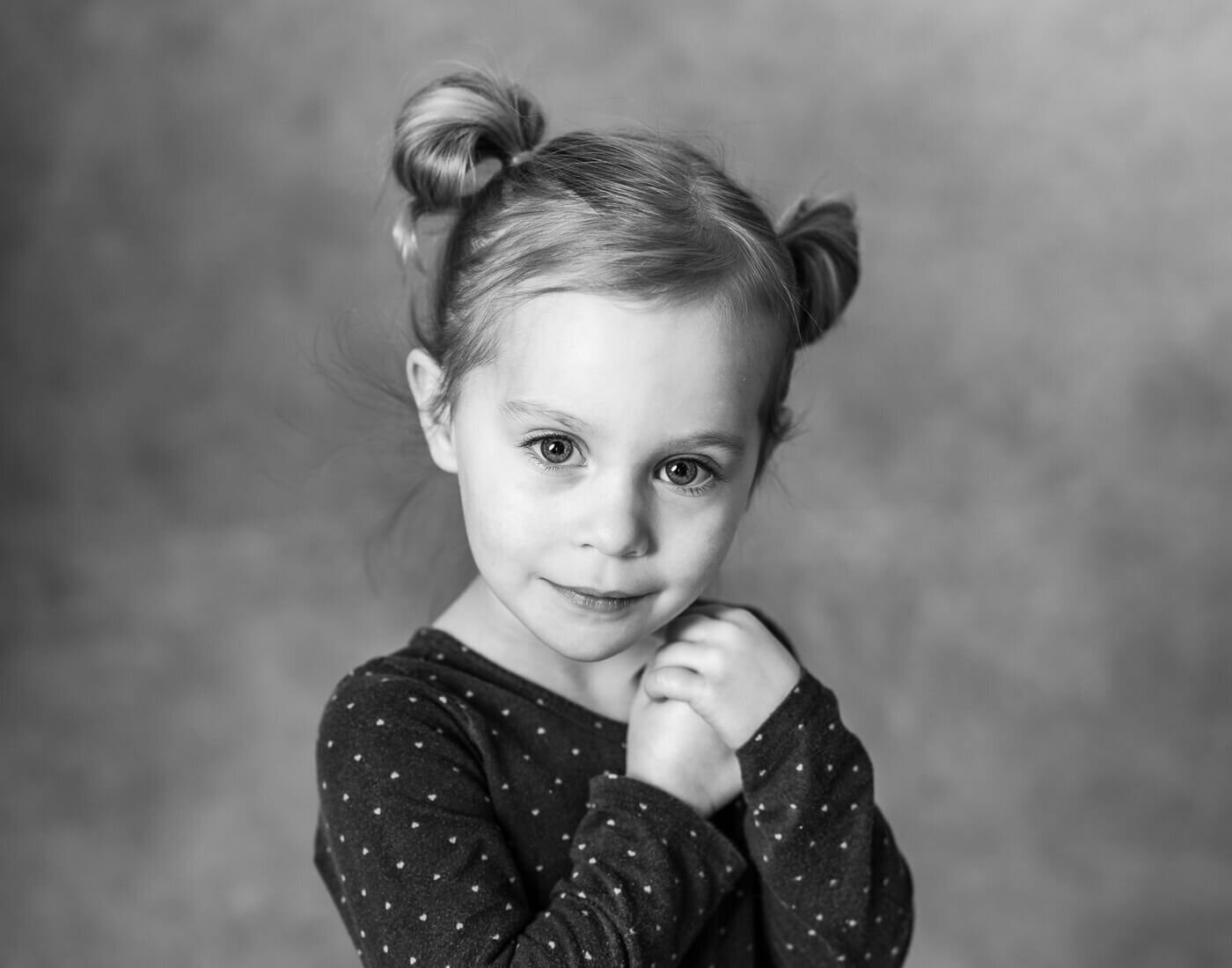 A young child poses, holding her hands together.