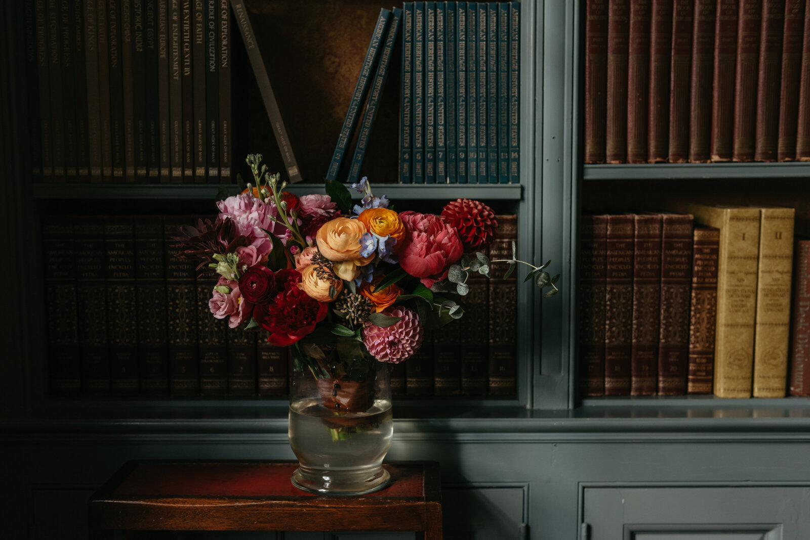 A colorful bouquet of flowers sits in front of a shelf of books