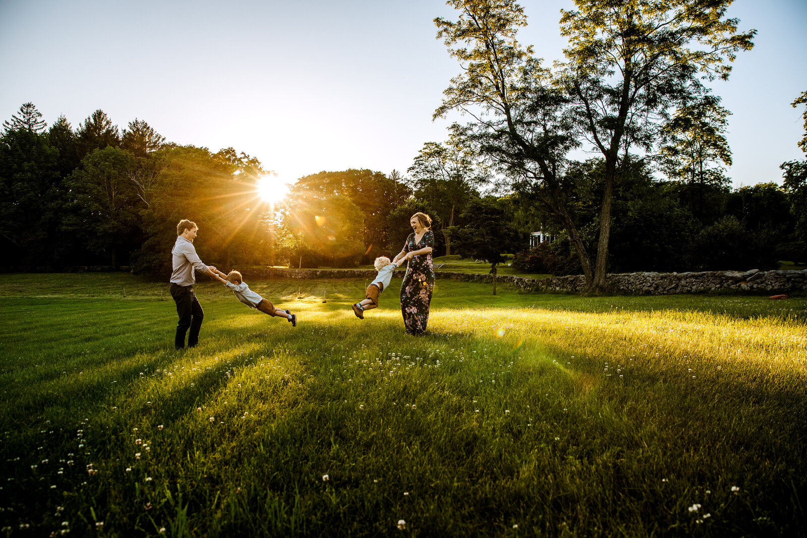 family of four swings boys in a boston field at sunset