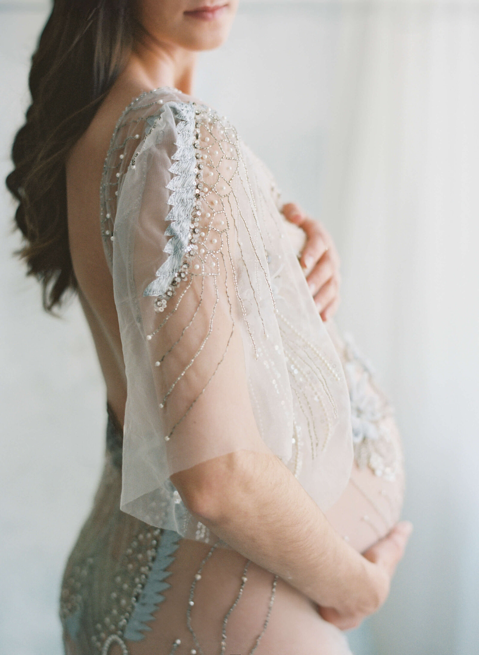 Expectant mother in a flowing gown, smiling warmly as she poses against a neutral studio backdrop.