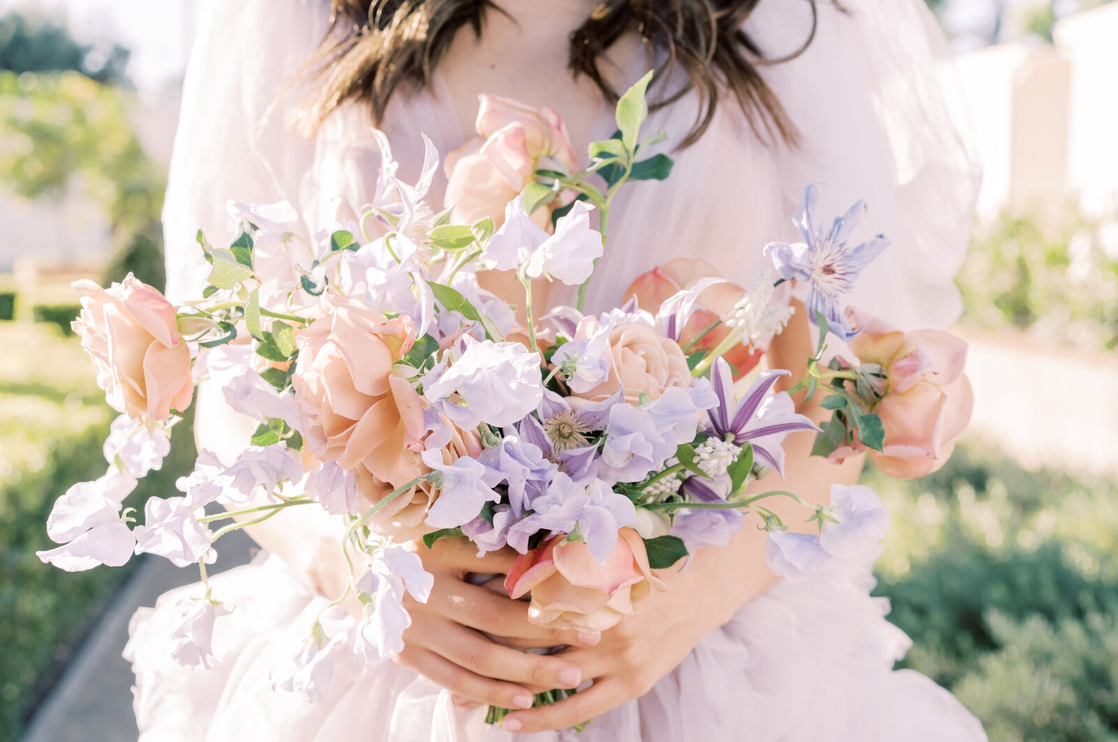 Portrait of a bride in a lavender wedding gown holding a bouquet of lavender and peach flowers.