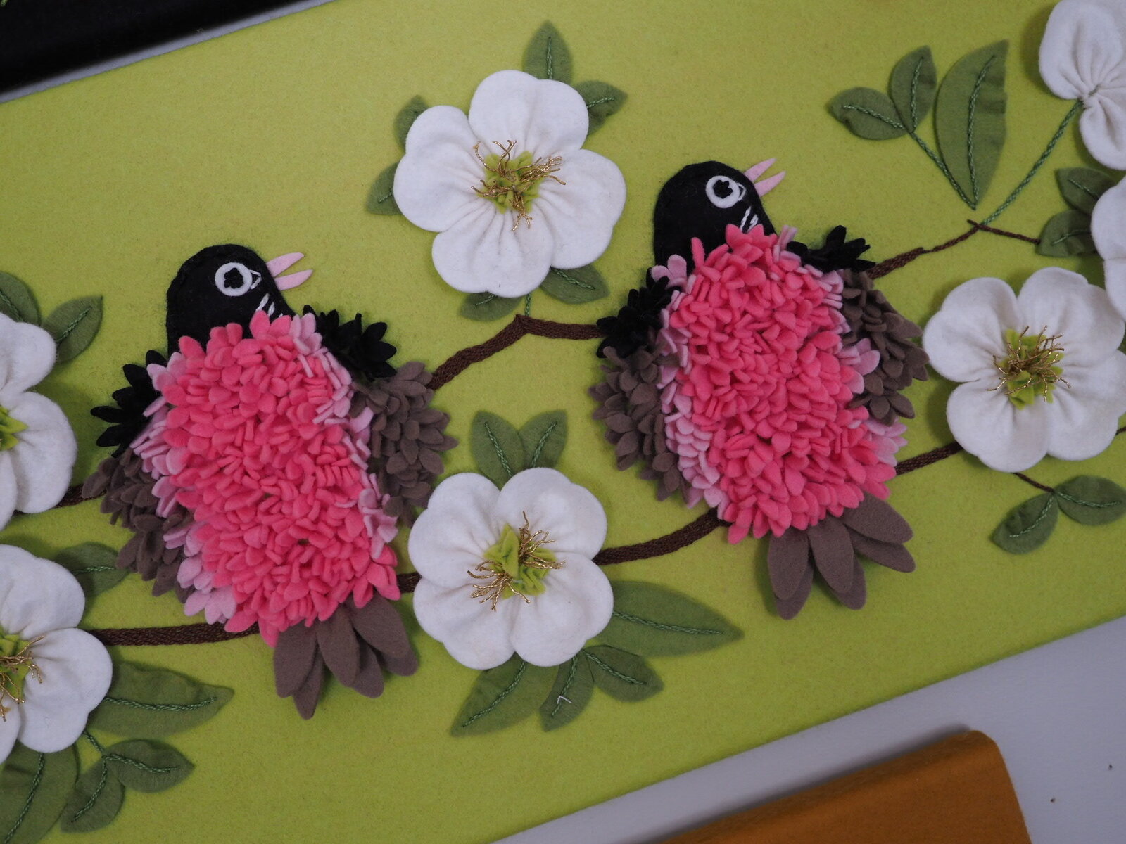 Two birds sitting on a branch with flowers all made out of felt and hand stitched.