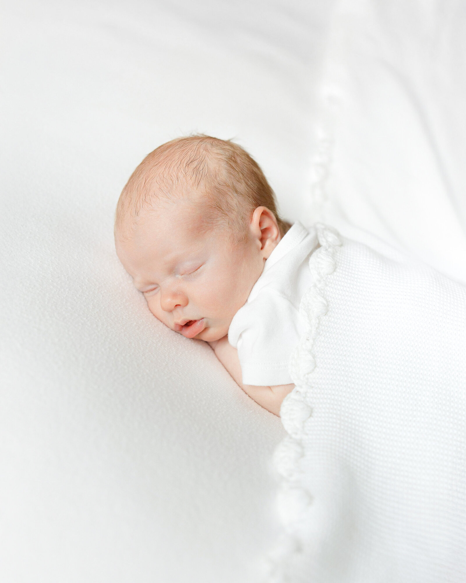 newborn sleeps on belly with textured white blanket