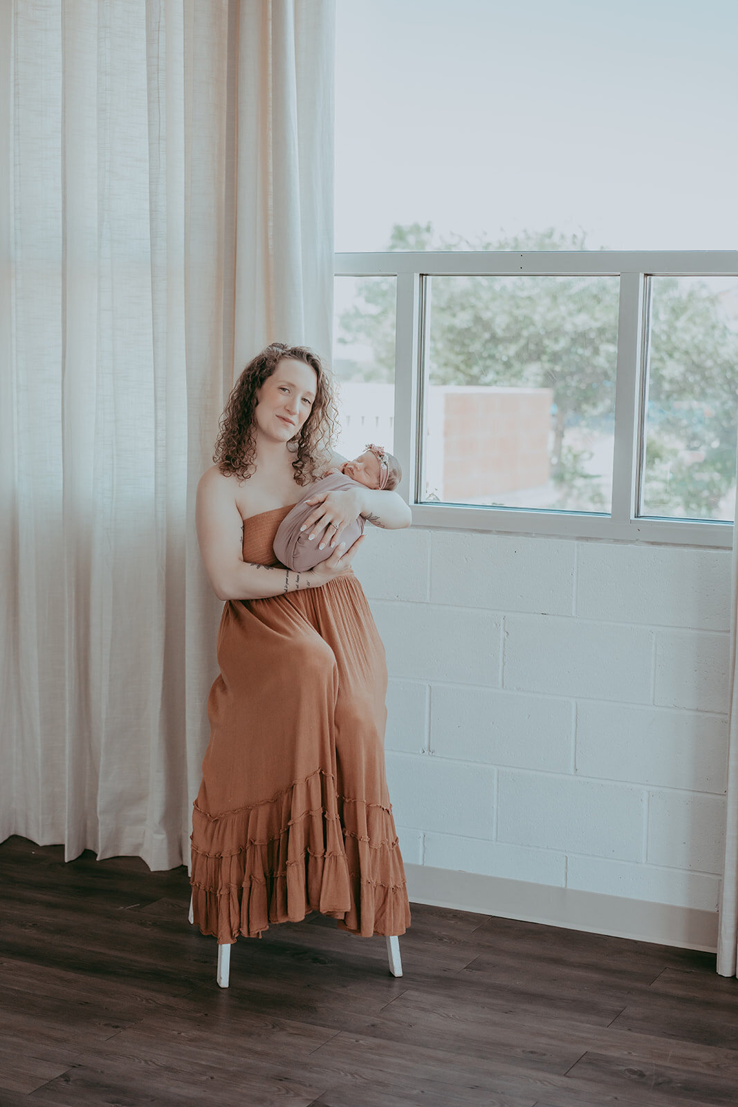 mom sits on still holding newborn near light filled studio in colorado