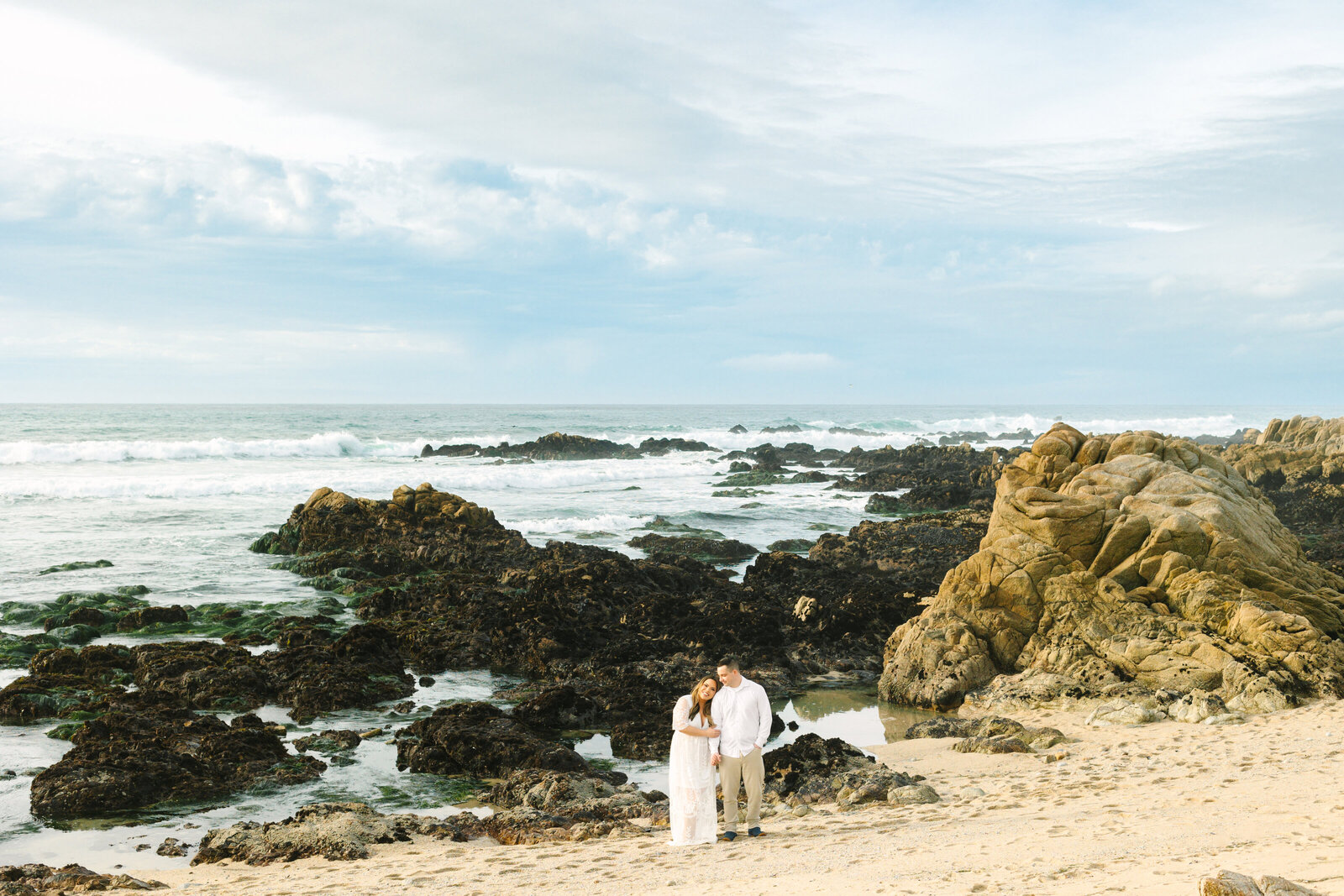 An engaged man and woman take photos on the beach in Pacific Grove, Monterey, California near Big Sur.