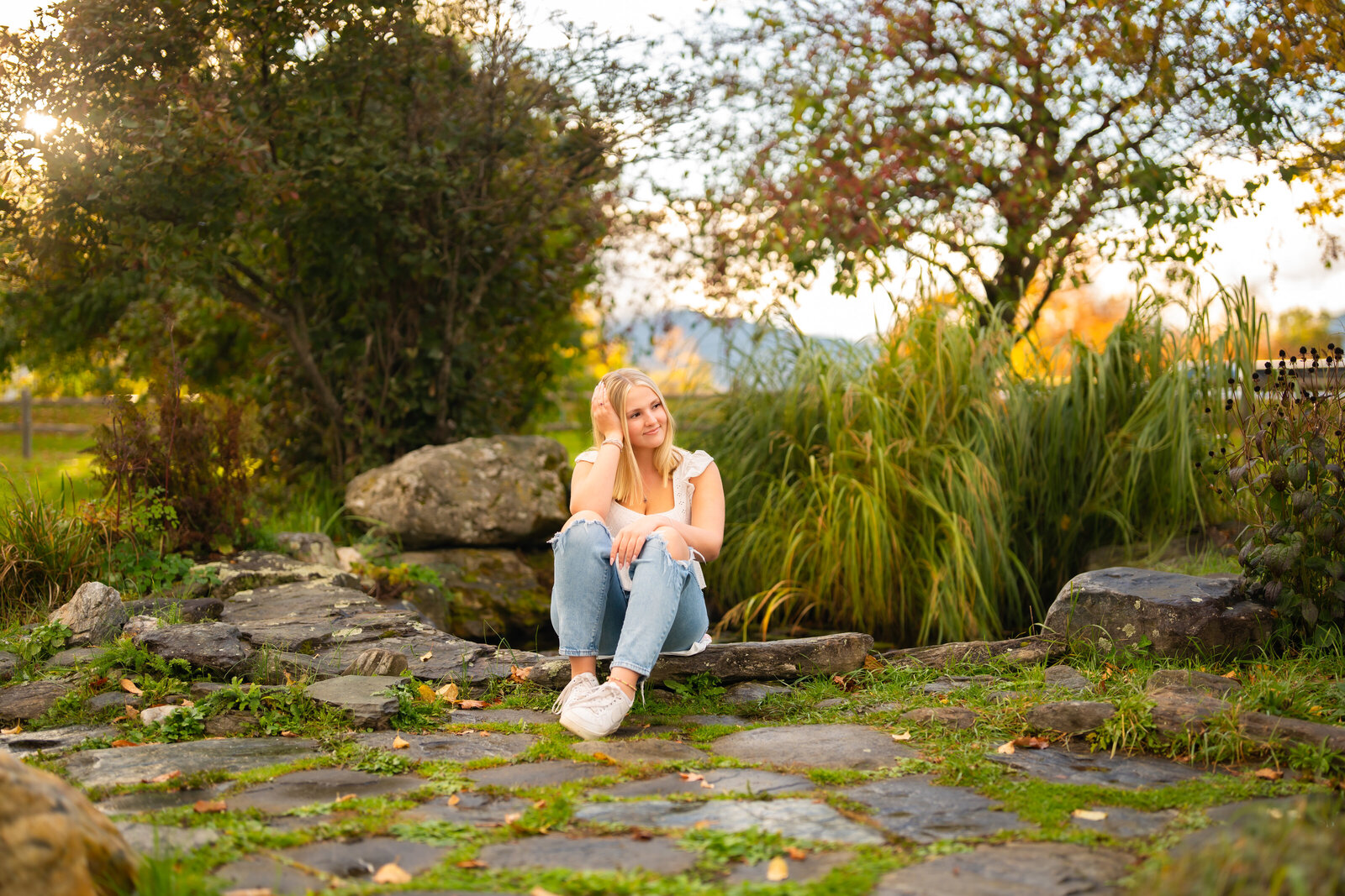 High school senior girl sitting on stone steps in a garden, surrounded by greenery.
