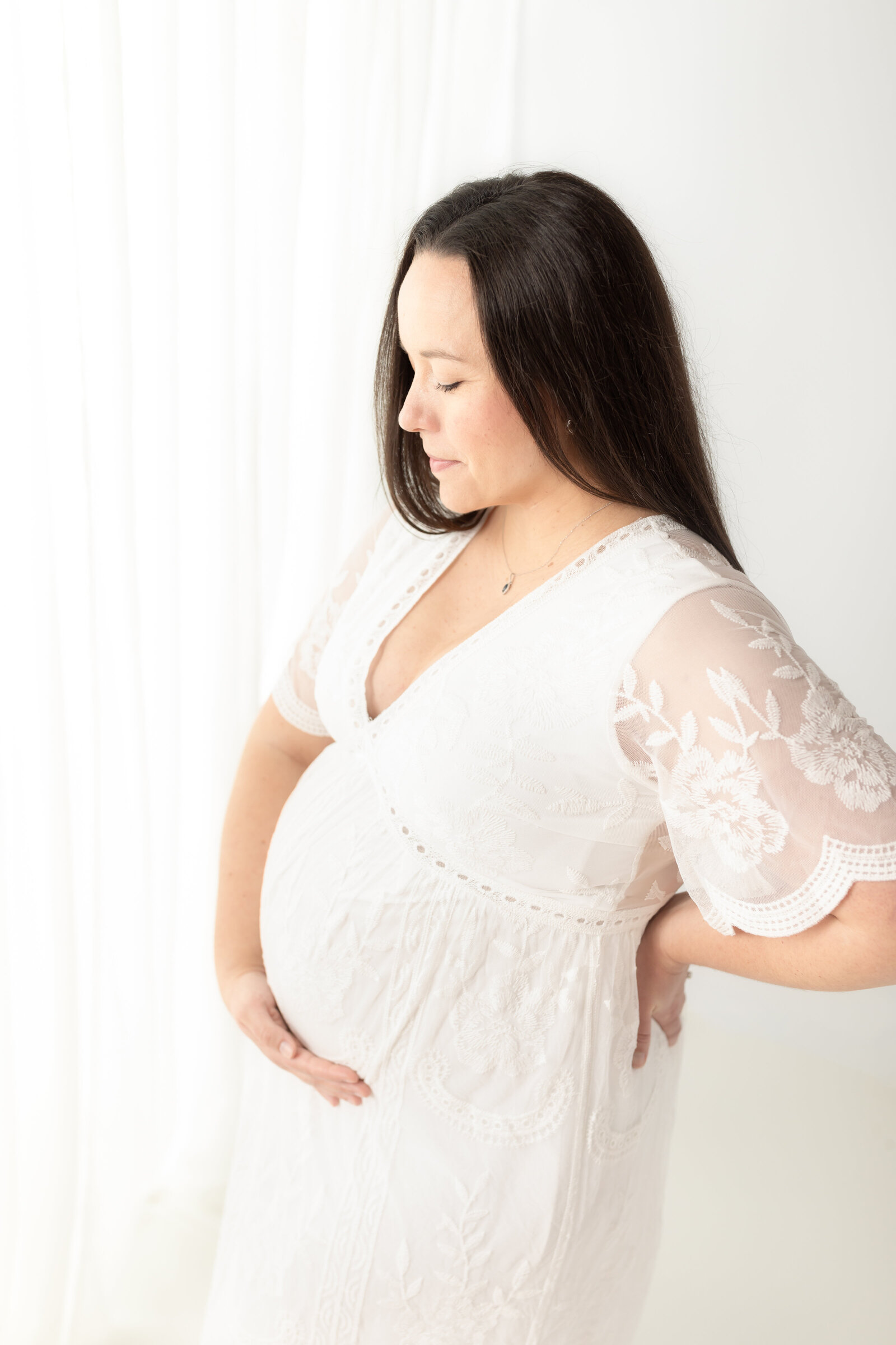 pregnant mother holding belly in white lace dress for maternity photoshoot Cleveland maternity photographer