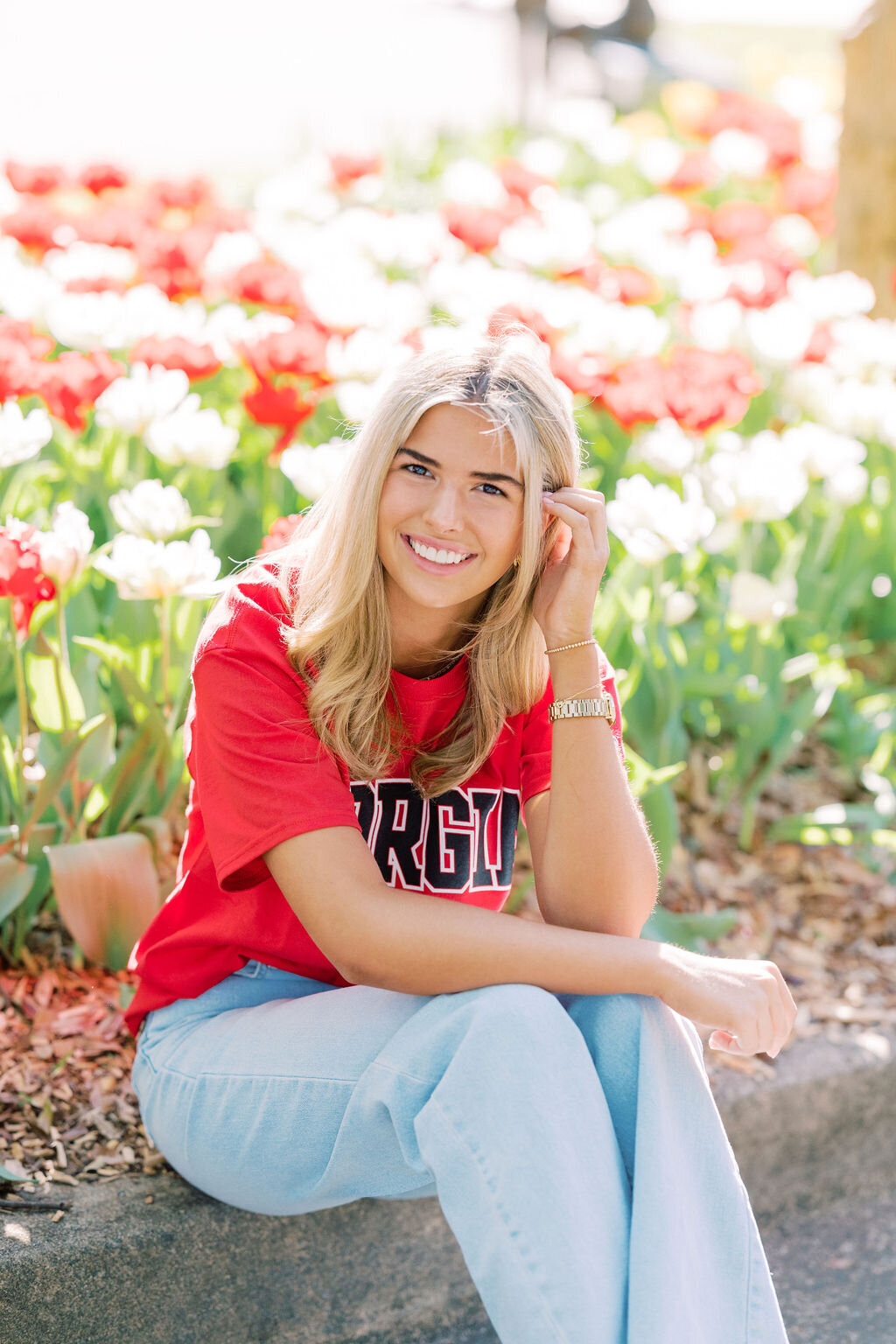 Girl wearing UGA shirt smiles with red flowers in background