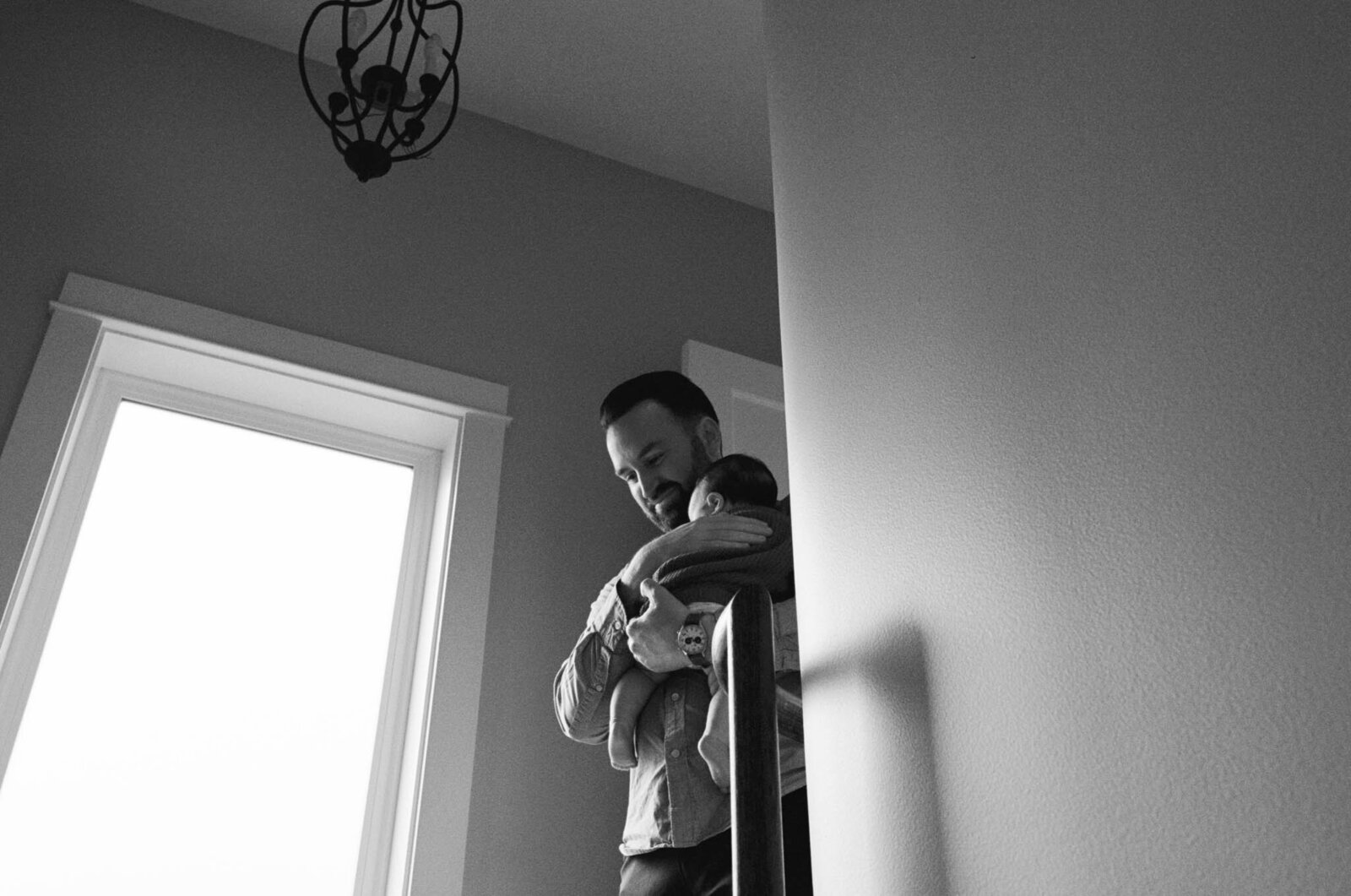 Dad walking down the stairs holding newborn baby girl in Portland, Oregon home.