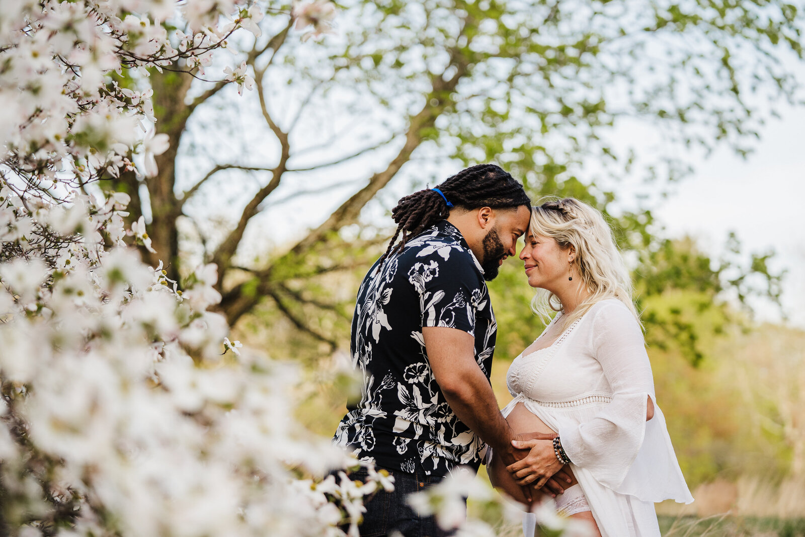 pregnant couple stands head to head in white blossoms