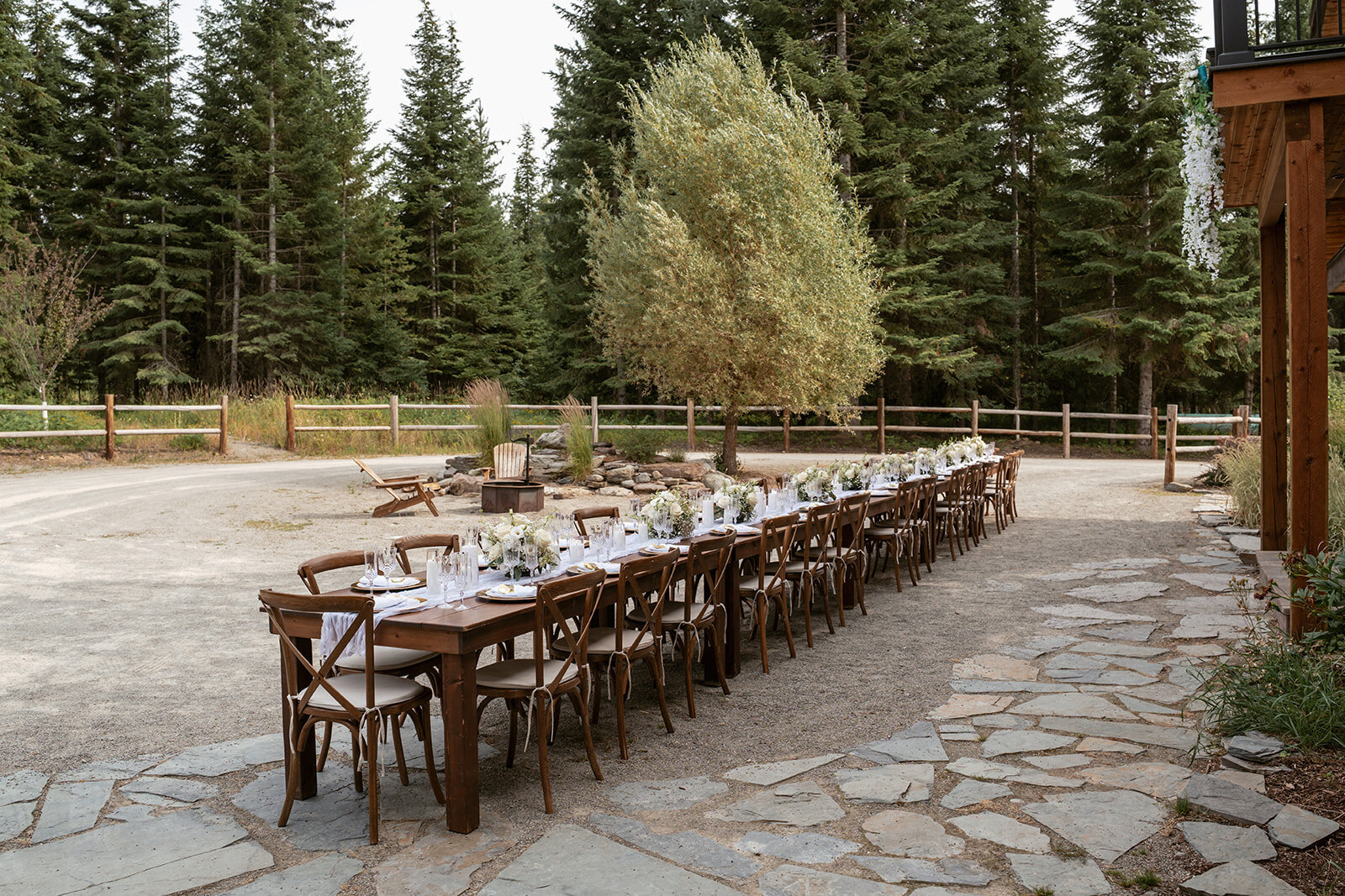 A beautifully styled long wooden table set with white linens and floral arrangements for an elegant outdoor elopement celebration.