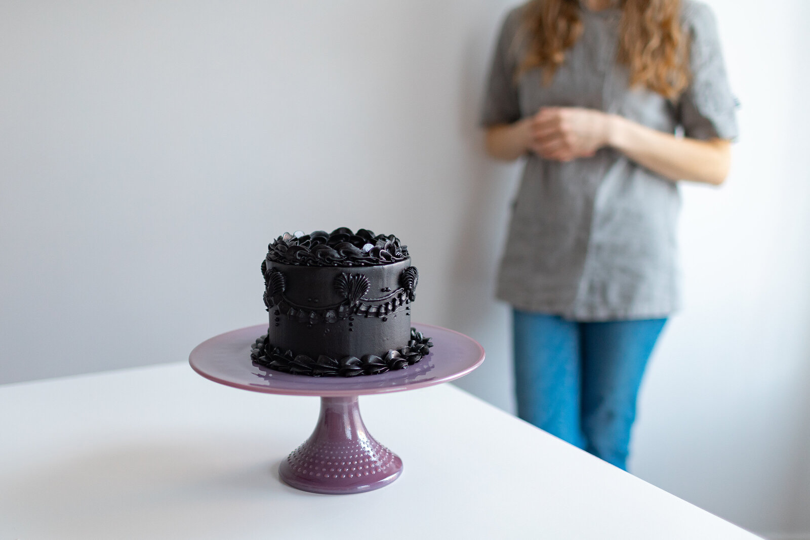 color image of black cake with baker behind her