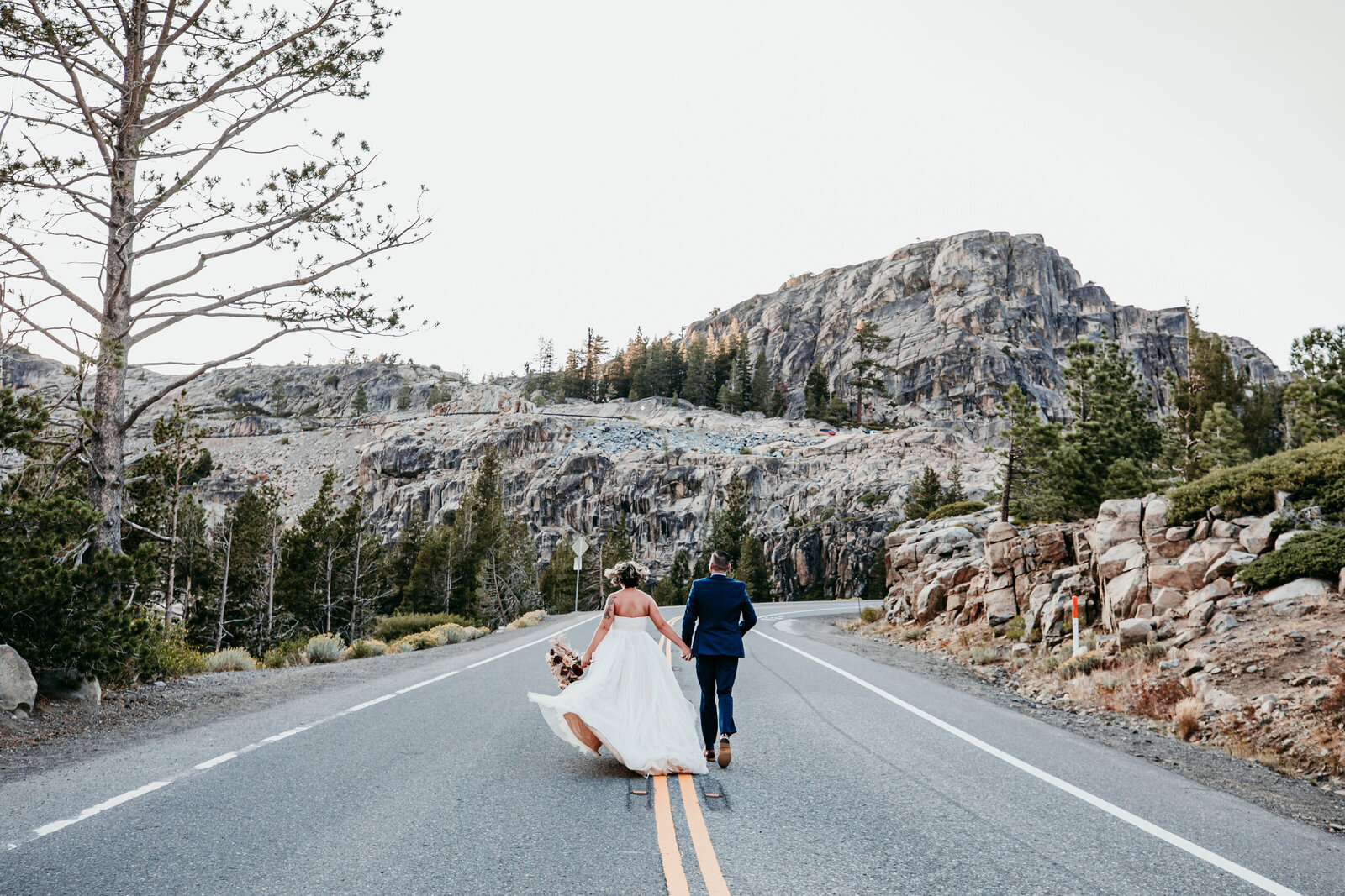 Bride and groom walking hand in hand down a winding mountain road near Donner Summit during their Lake Tahoe elopement