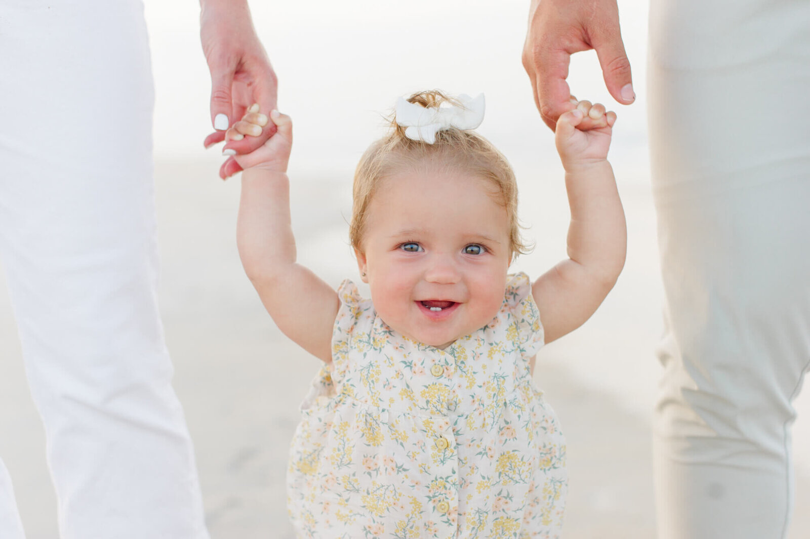Closeup photo of a young girl holding mom and dads hands while walking on the beach