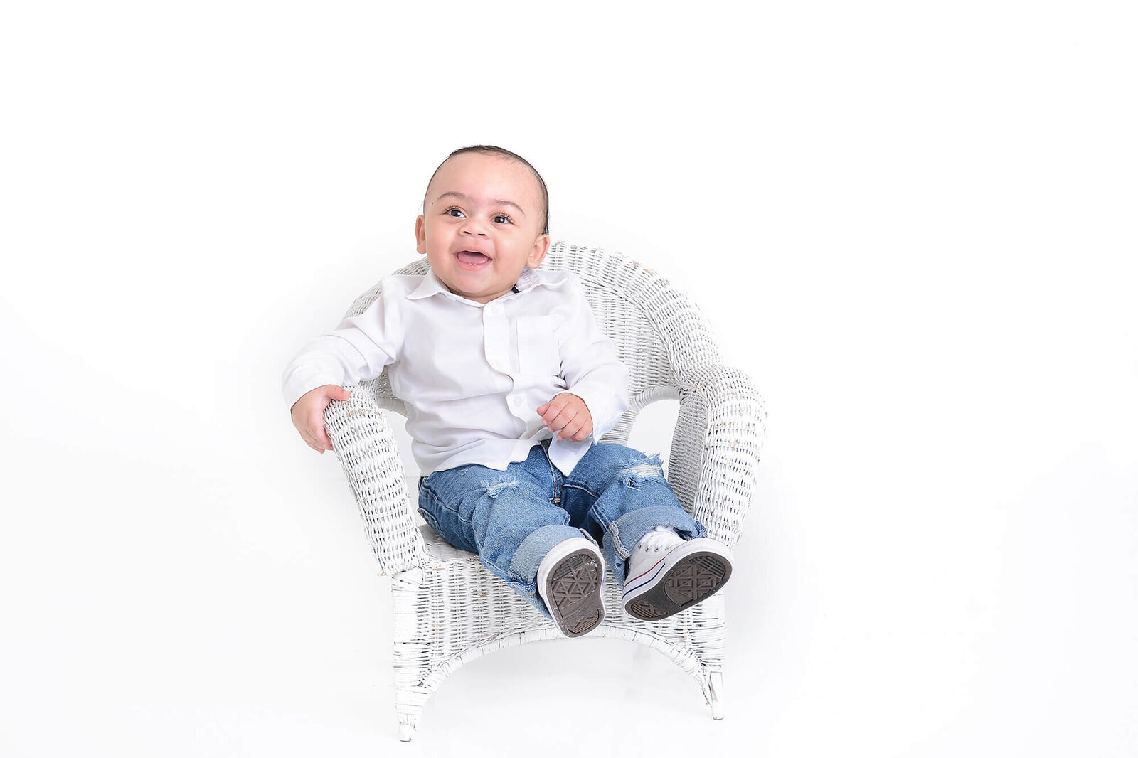 a one year old sits on a white bench and smiles at the camera