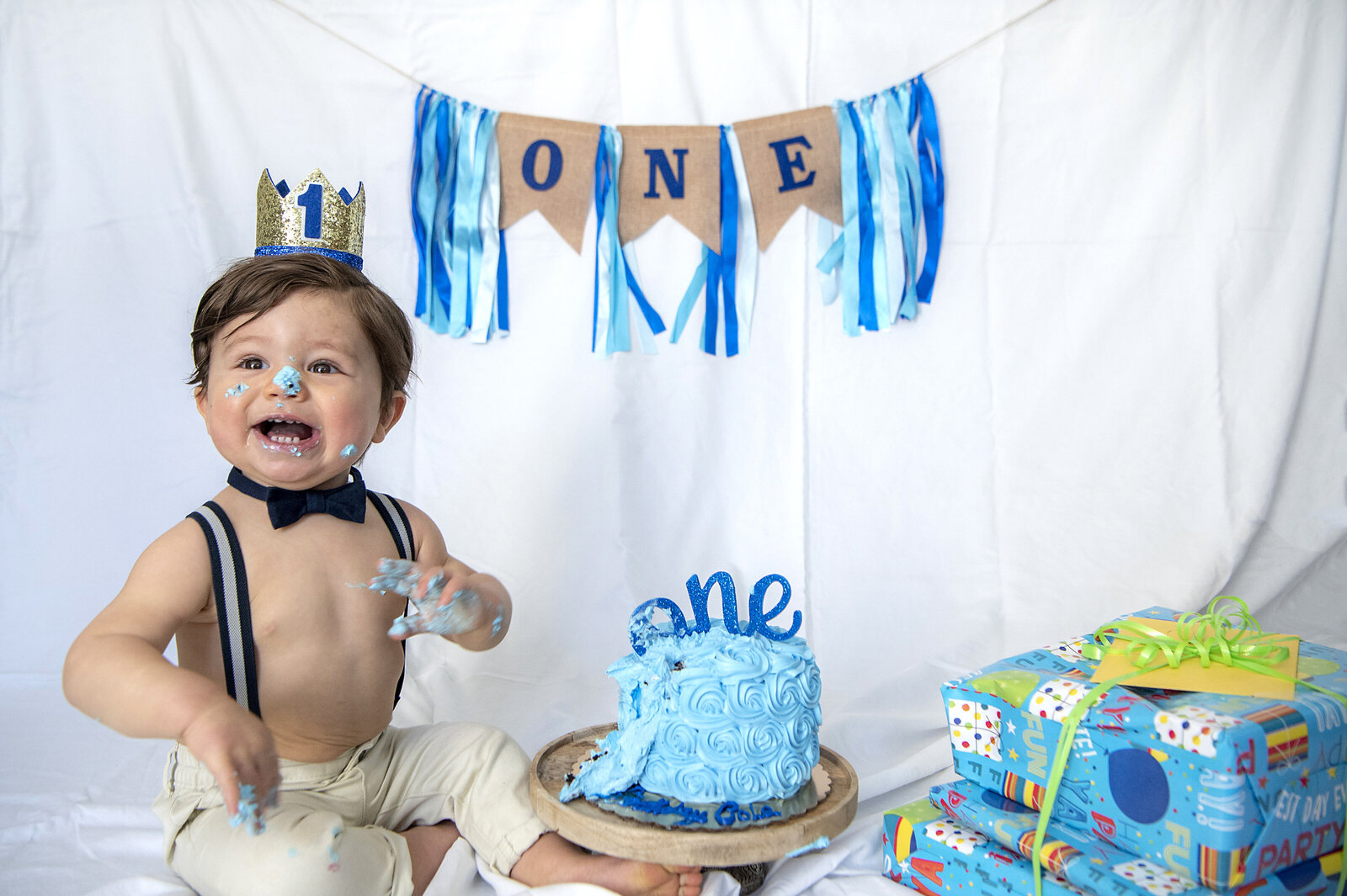 A small child laughing with icing on their hands and face from a cake in front for their first birthday 