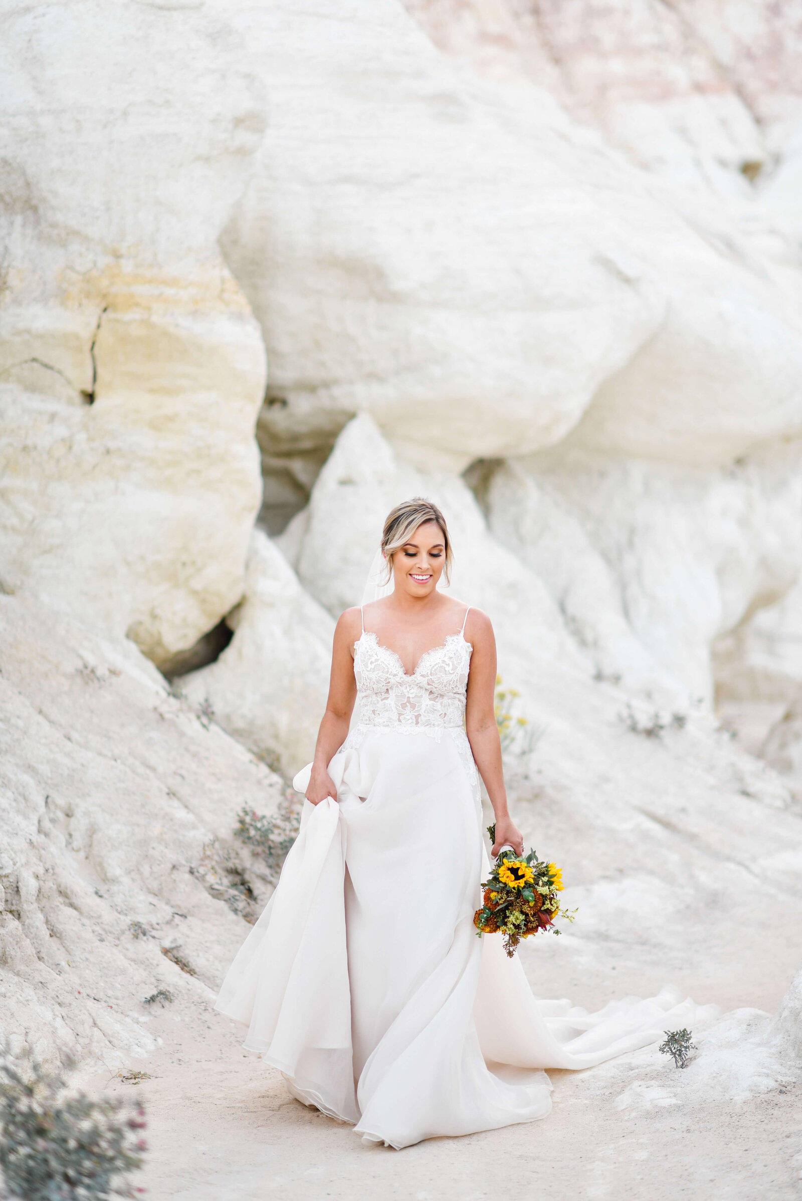 Lovely bride holds up her dress and walks along a sandy area in an image taken by Virginia wedding photographer Erin Winter