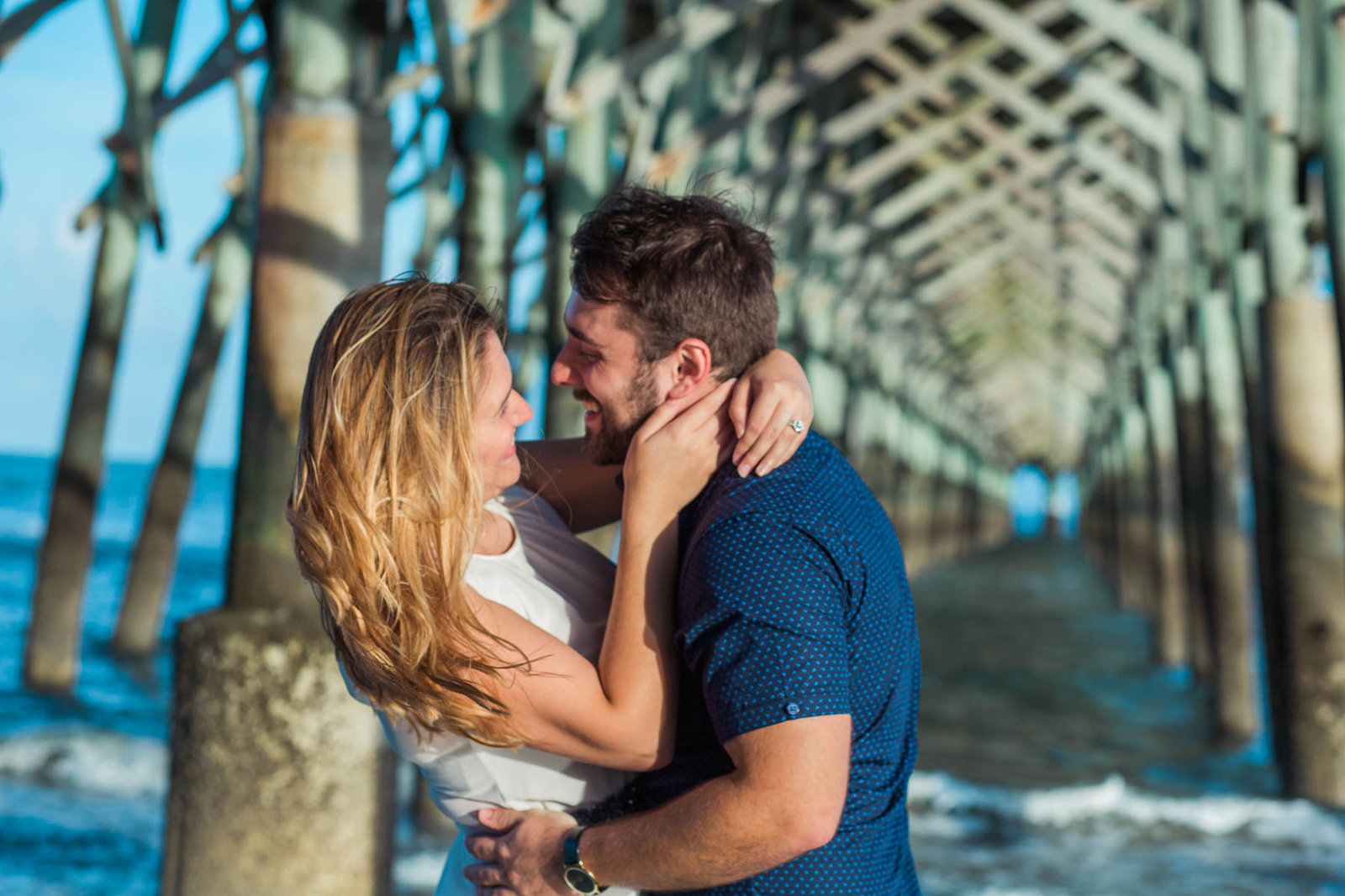 Engaged Couple hugging under fishing pier, Folly beach in Charleston, South Carolina