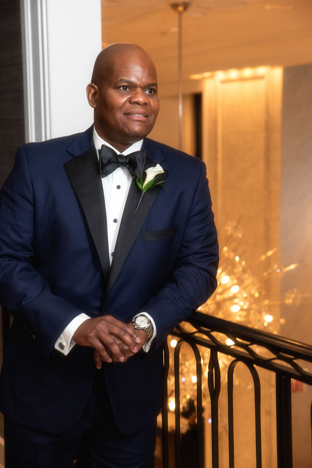 A man in a tuxedo and bow tie is standing on a balcony
