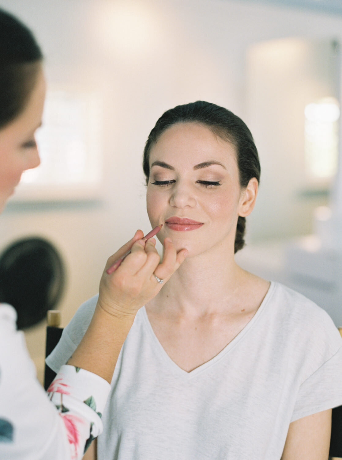 A bride in a white t-shirt gets her makeup done.
