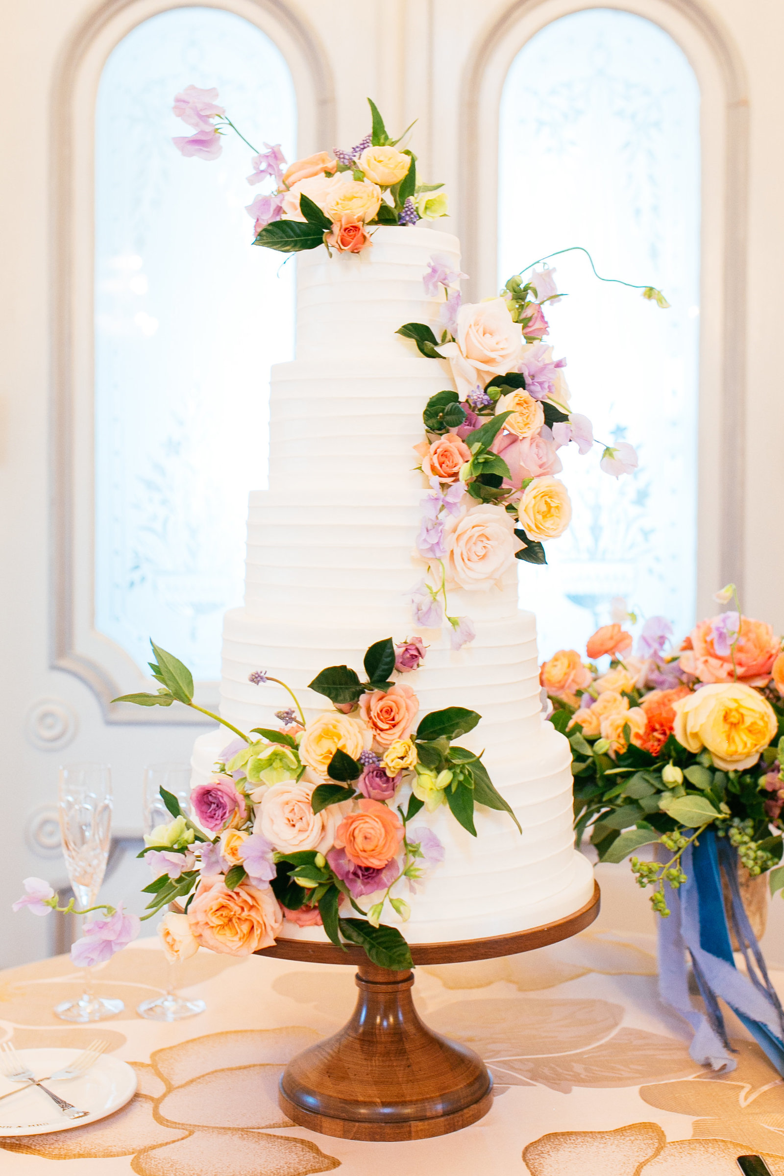 Simple and stylish white textured buttercream wedding cake with colorful summer flower cascade at Merrimon Wynne House