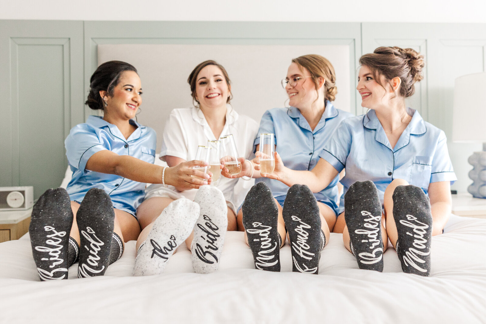 a bride and her bridesmaids show off their socks while cheersing their drinks