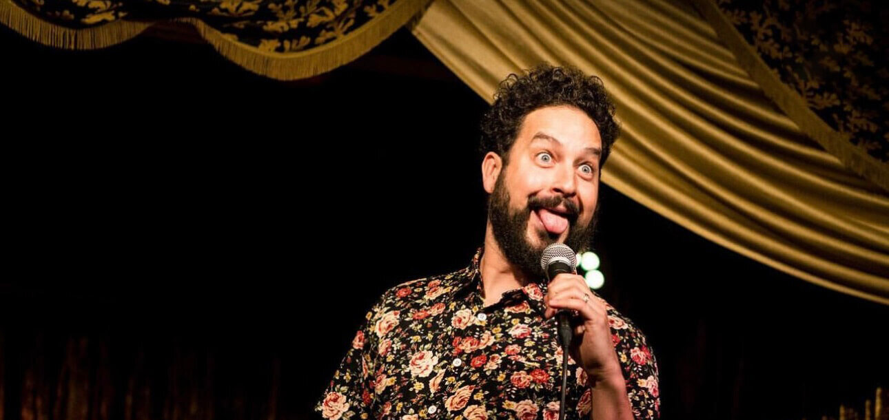 Ahmed Bharoocha on stage, holding a microphone, and sticking his tongue out