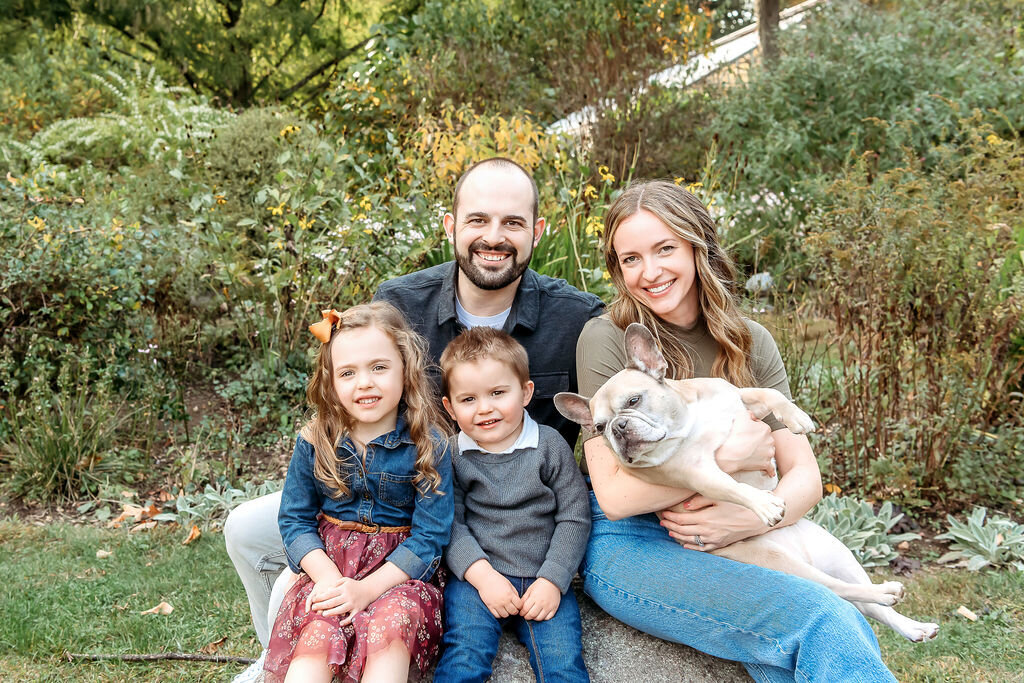 Connecticut Family Photographer documents a family portrait featuring parents with two young children and their French Bulldog, sitting together in a lush garden setting