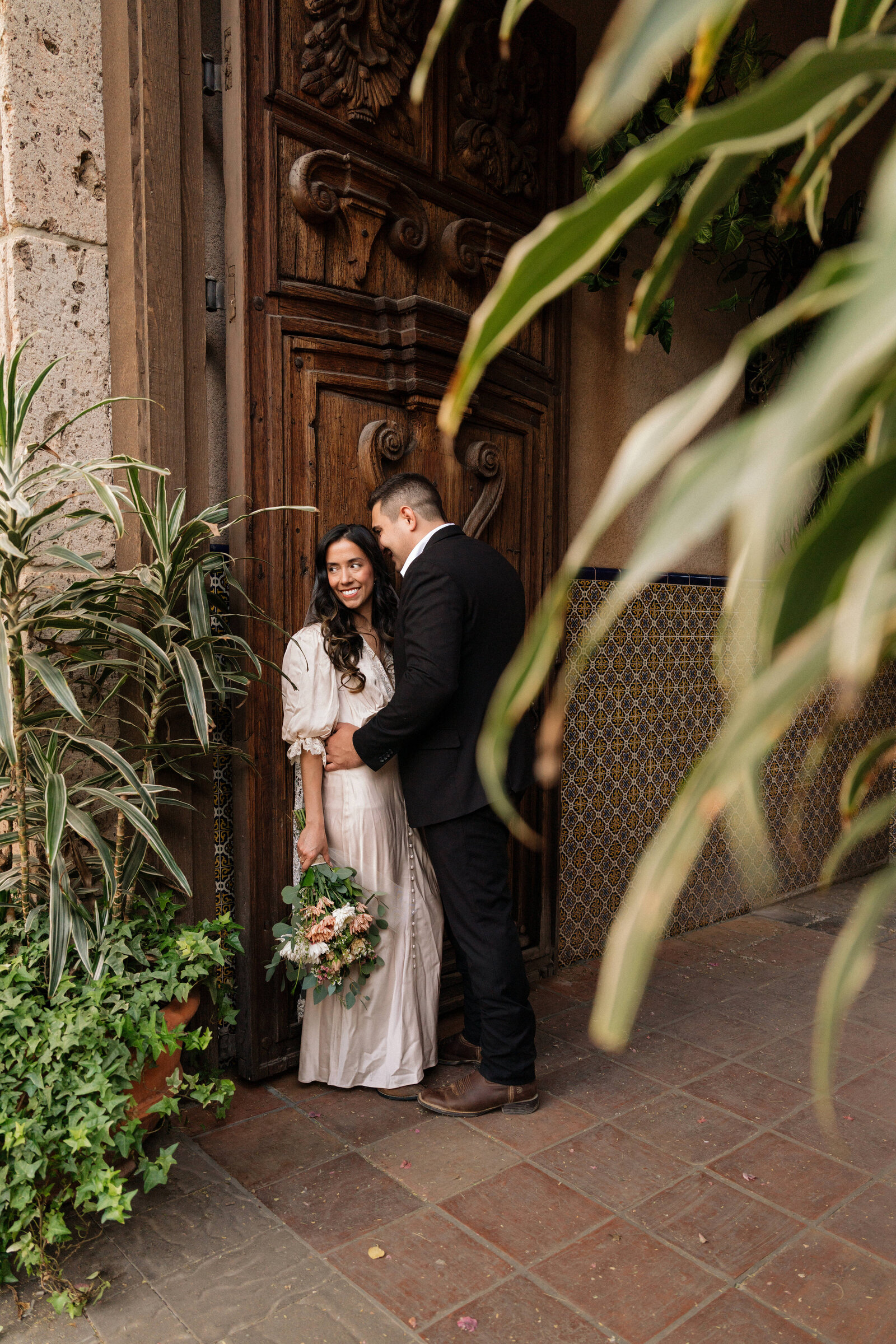 Bride and groom sharing an intimate moment in front of an ornate wooden door at Tlaquepaque Arts & Shopping Village in Sedona during their romantic elopement.