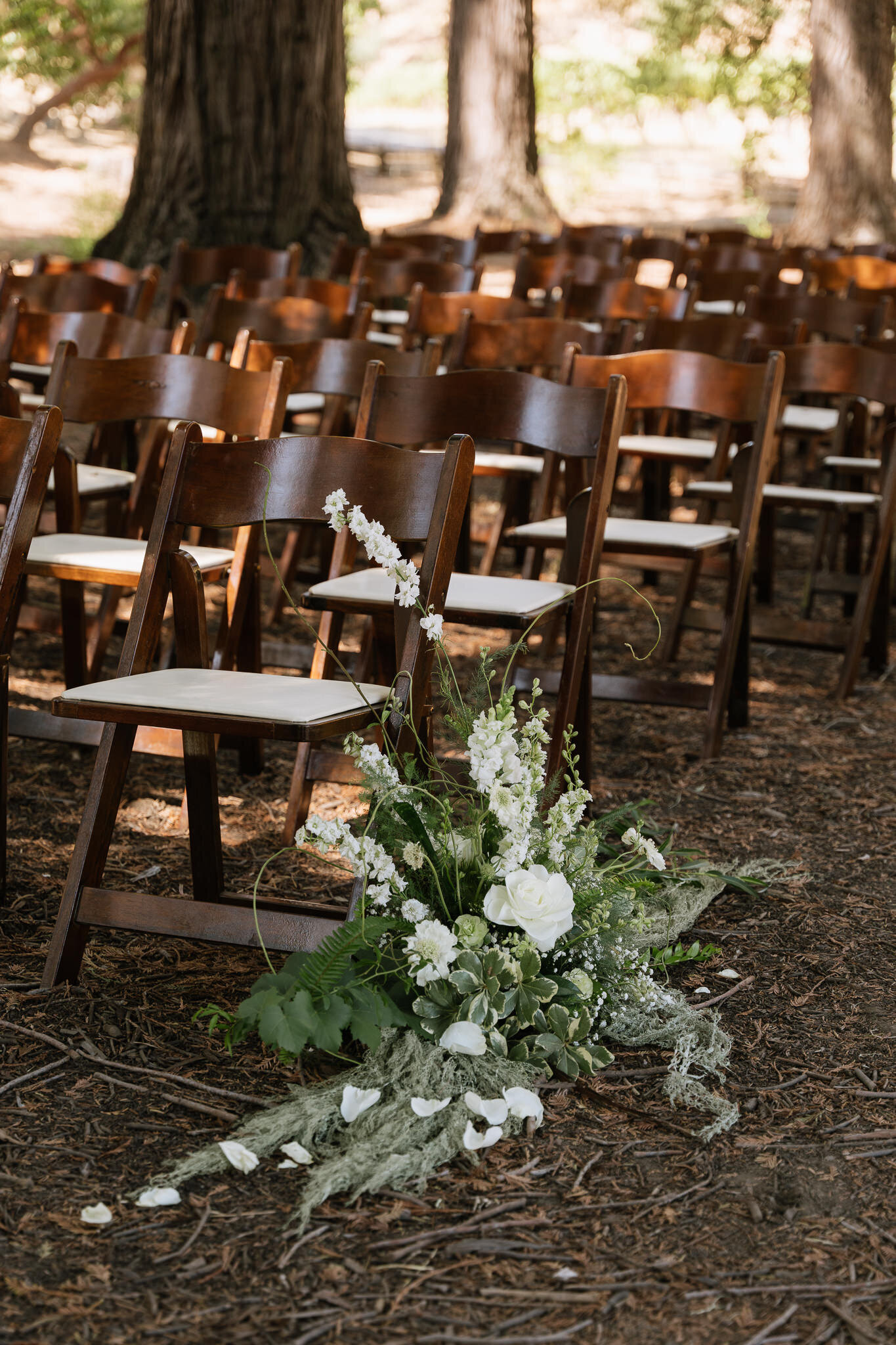 White floral details with wooden chairs under towering redwoods for outdoor wedding ceremony in Northern California