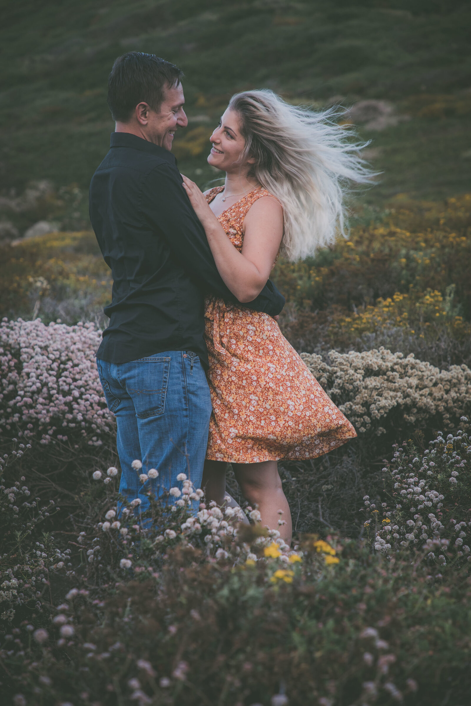Couple faces each other and smiles among wildflowers in Big Sur.
