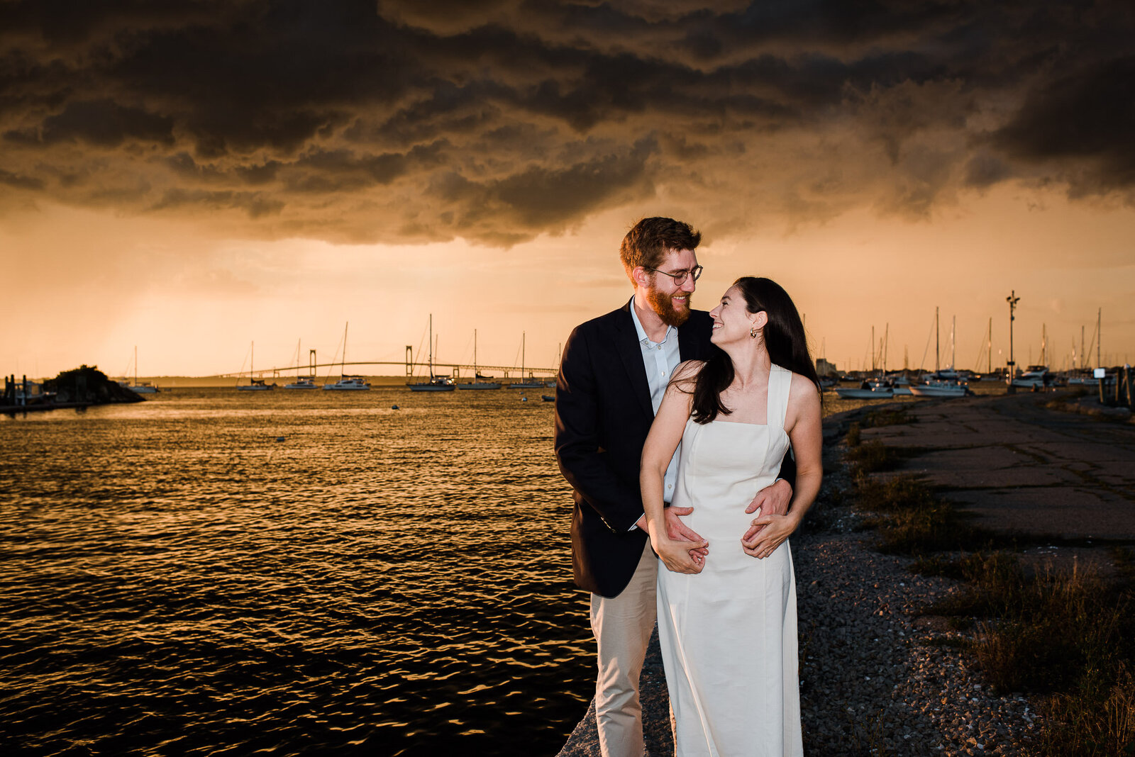 couple embrace back to front in front of water with dramatic  clouds