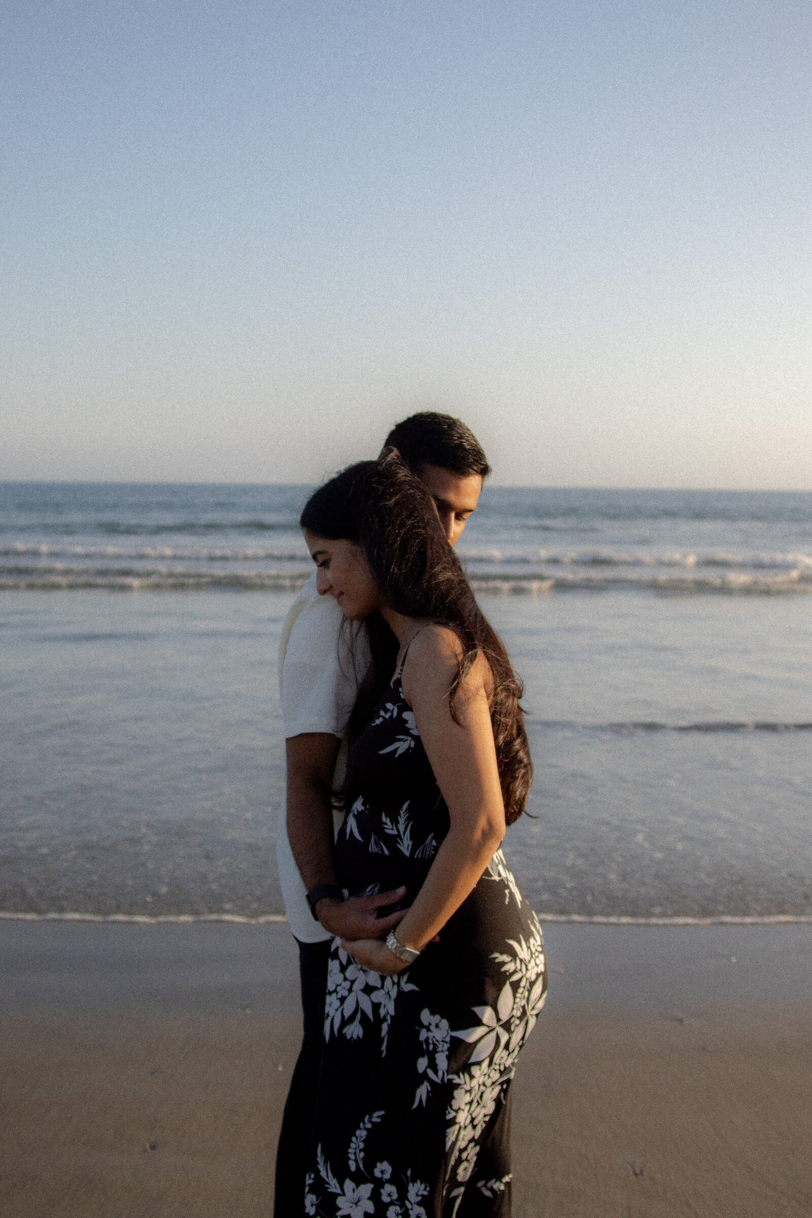 Expecting mom and dad embrace on beach while dad caresses mom's belly