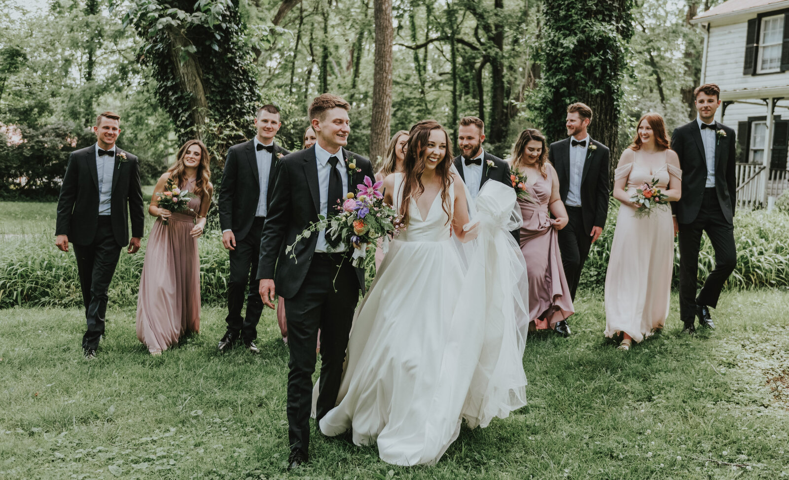 A bride and groom walk with their wedding party through the woods