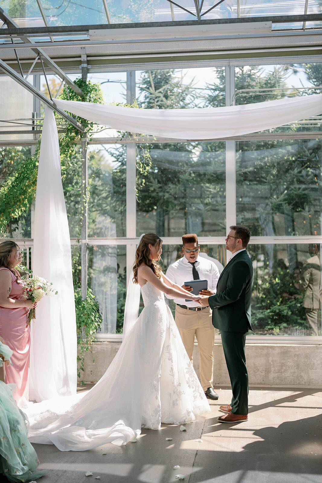 Bride and groom exchanging vows under flowing drapery in a greenhouse ceremony at a Michigan wedding.