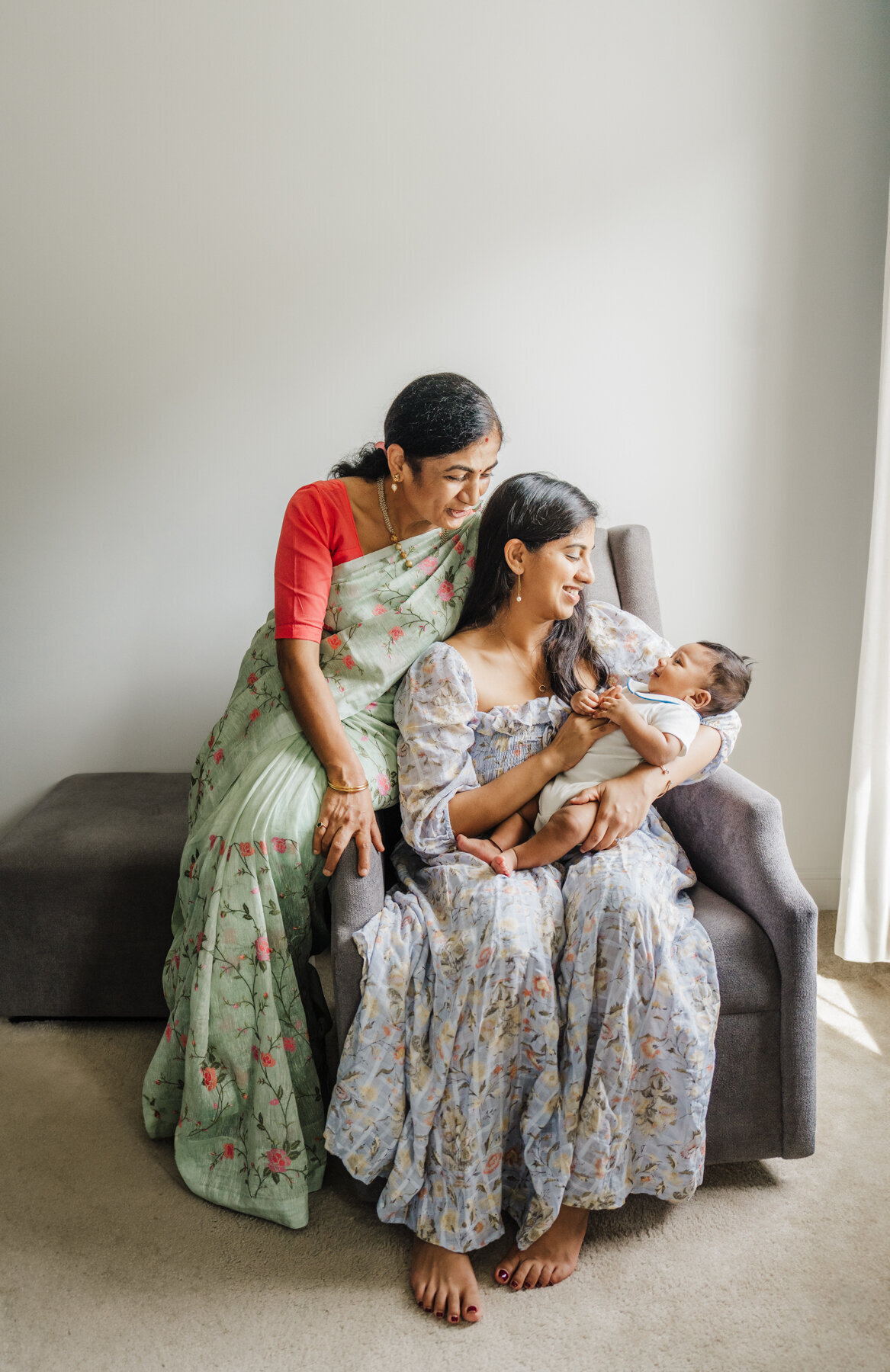 mother and grandmother in traditional Indian dress stare down at newborn baby boy