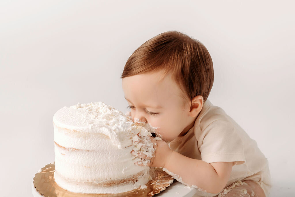 Baby diving into white frosted cake during adorable first birthday cake smash photography session