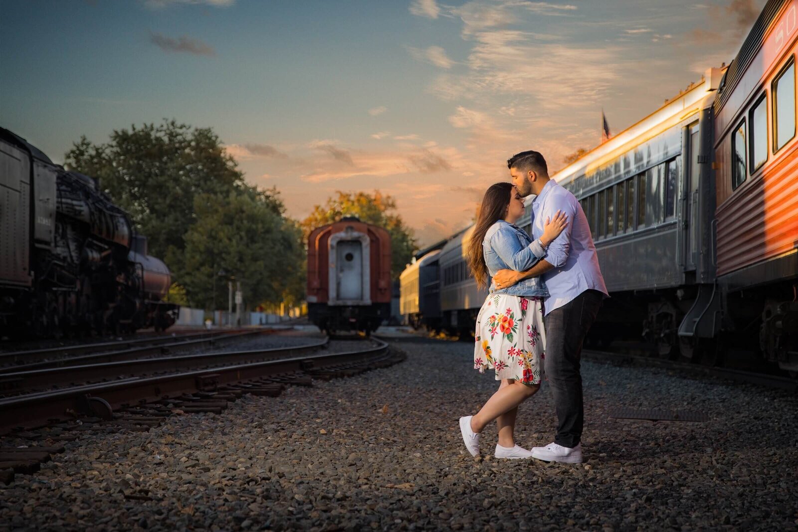 Engaged couple poses in the Old Sacramento train yard. Groom kisses bride's forehead while they are standing together. Photo by wedding photographer sacramento ca, philippe studio pro