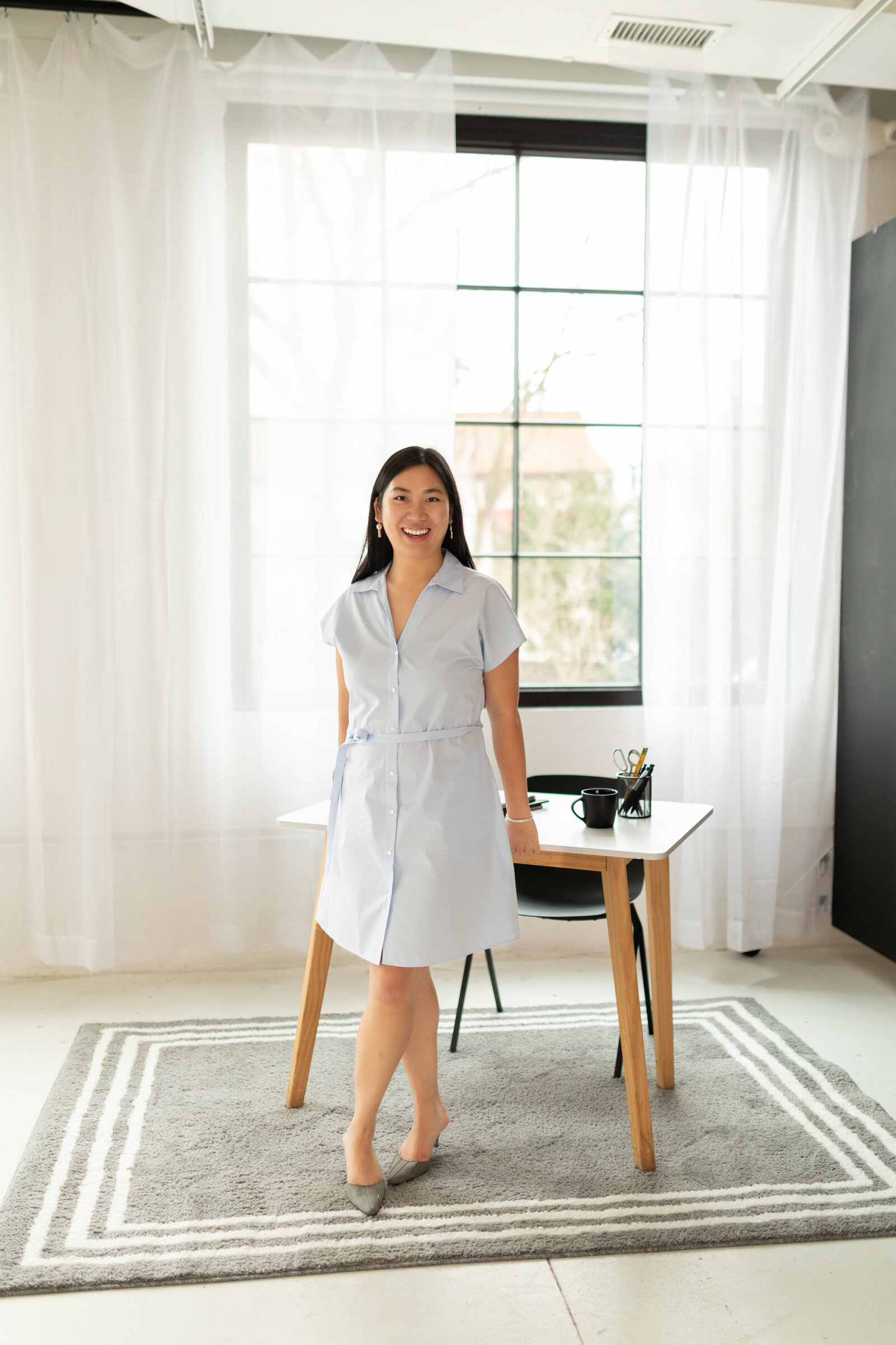 woman stands in bright studio against desk smiling at camera