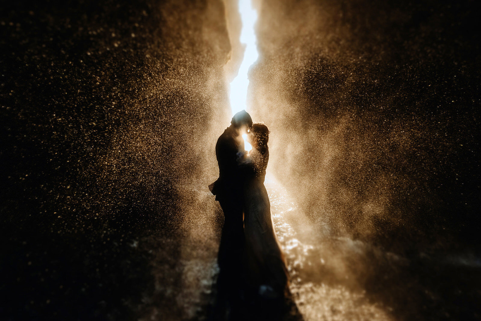 married couple is standing in warm epic lights under a waterfall in Iceland at their elopement