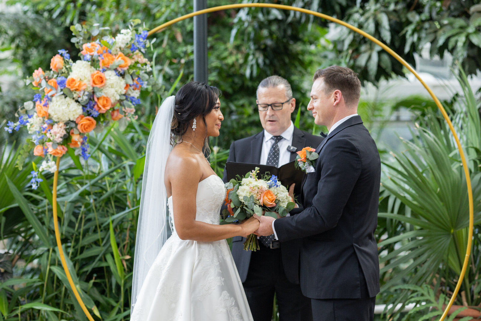 Bride and Groom saying vows at University of Georgia Botanical Garden in Athens Georgia. Bride is wearing a white long ball gown and groom is wearing a black tuxedo. 