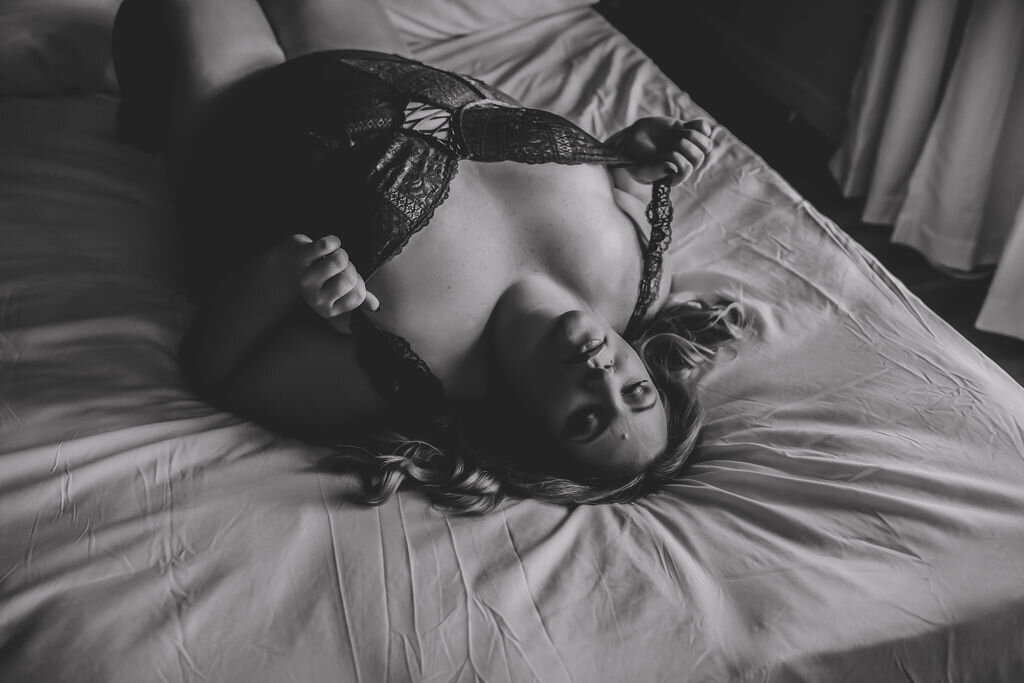plus size black and white boudoir image of woman laying on bed in lingerie